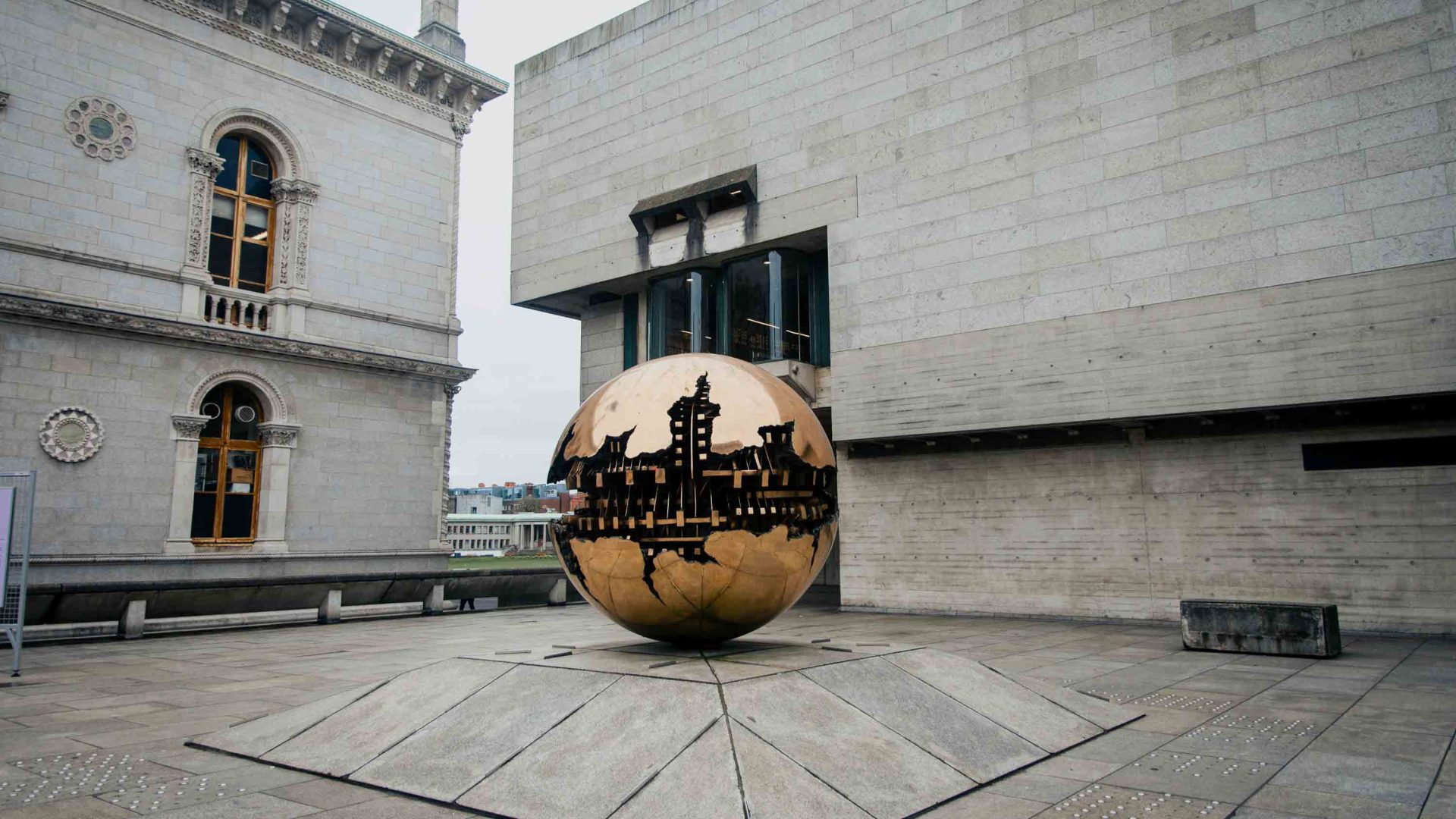 A spherical reflective sculpture in a courtyard.