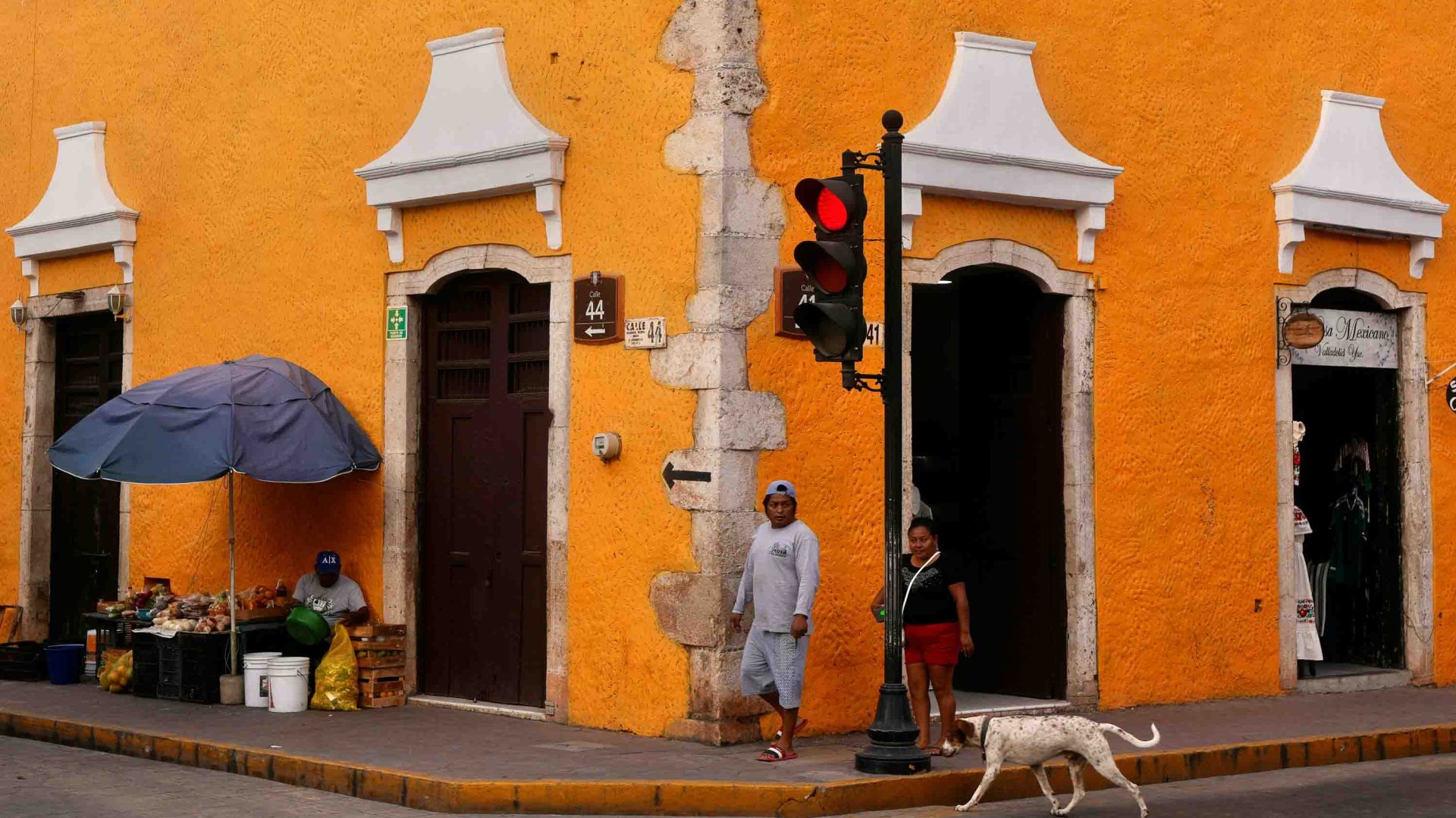 A man walks past an orange building where a vendor also sits.