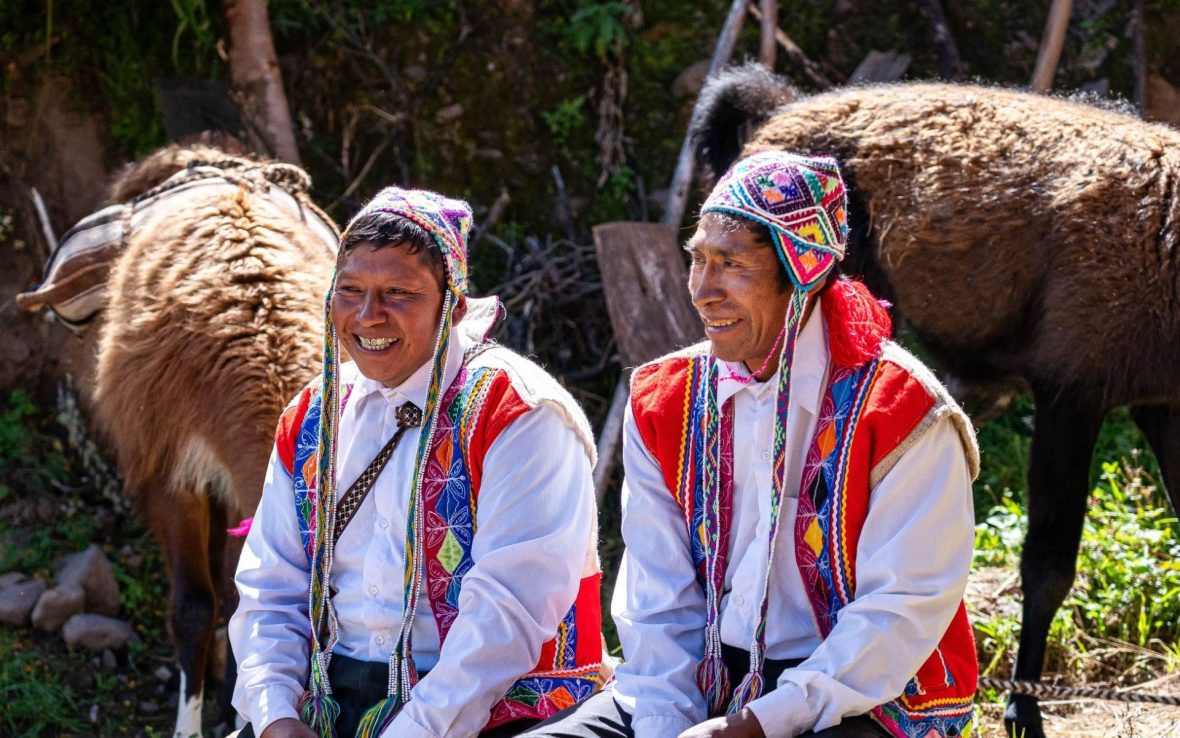 Two men in traditional Andean clothing sit and laugh together