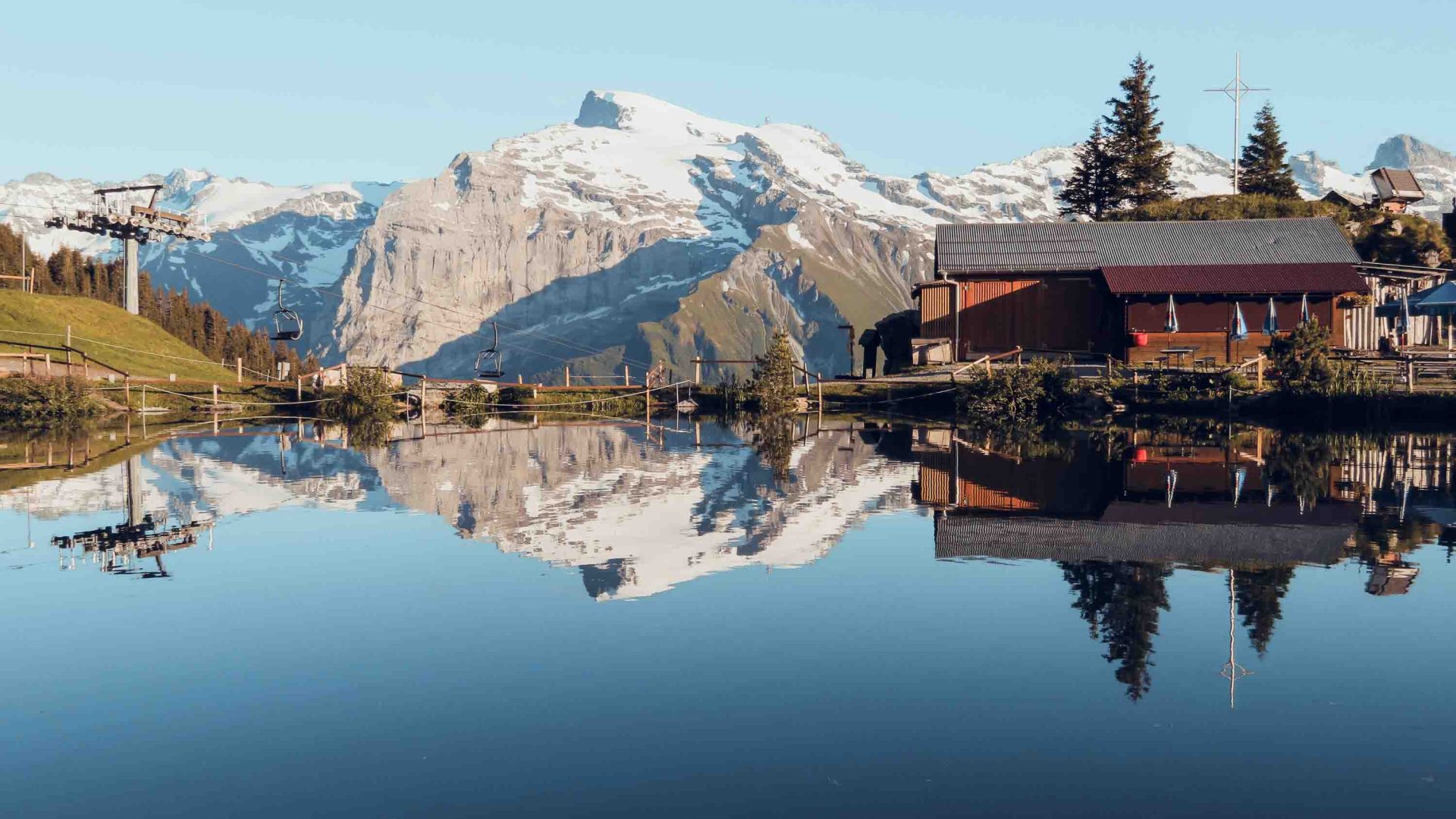 A hut and mountains are reflected in the still water of a lake.