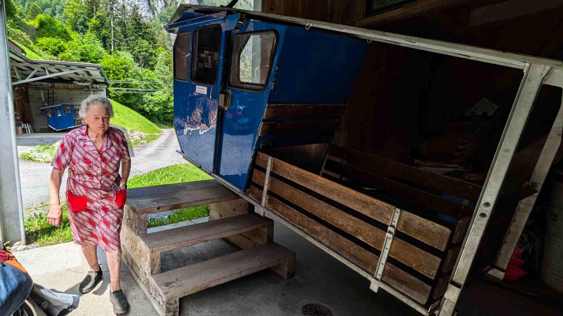 A woman in a red dress stands alongside an old cable car.