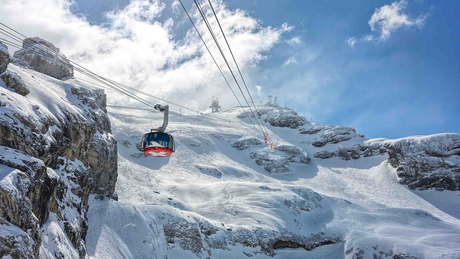 A red cable car in snowy mountains.
