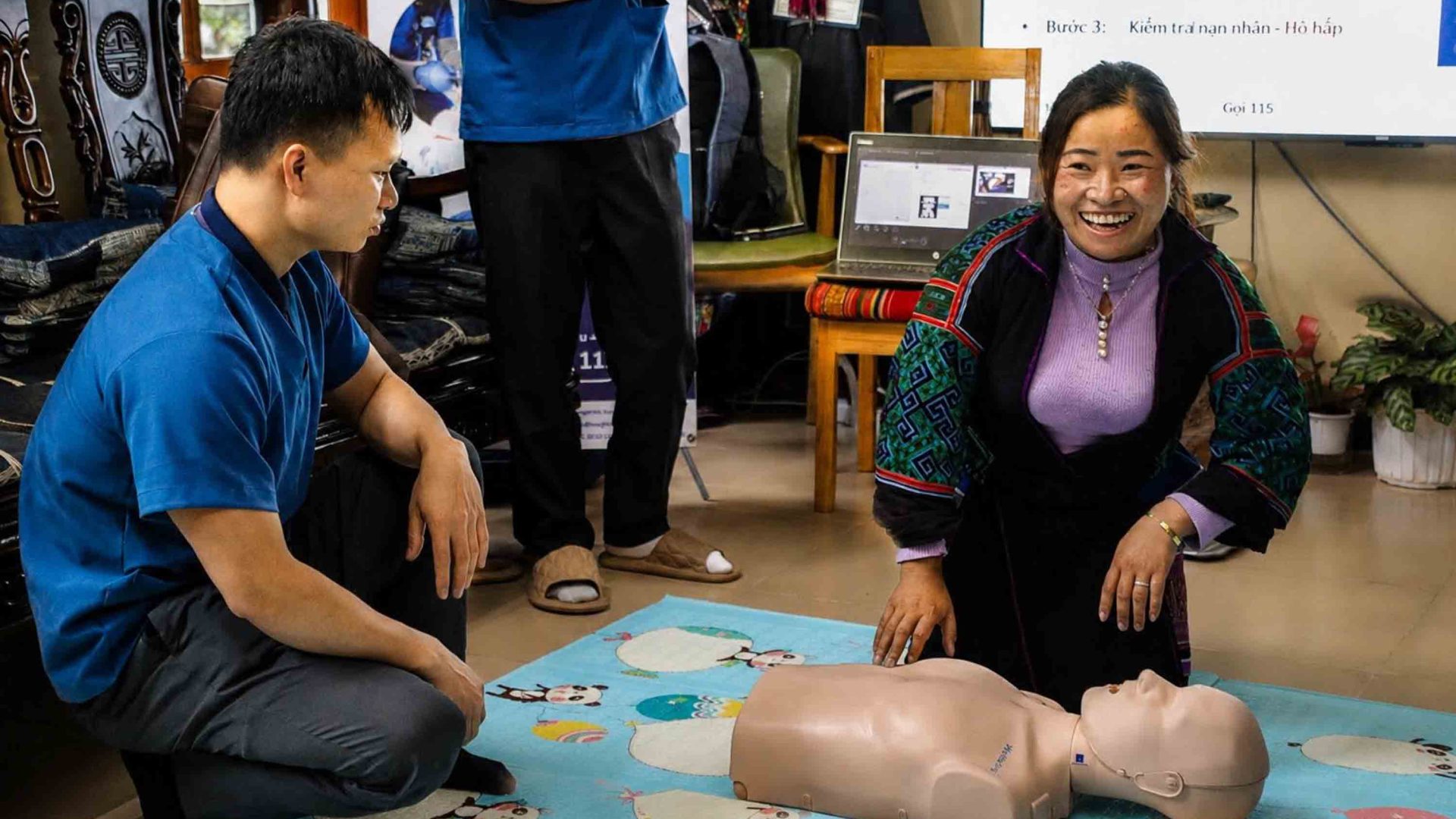 A woman smiles as she kneels by a resuscitation doll.