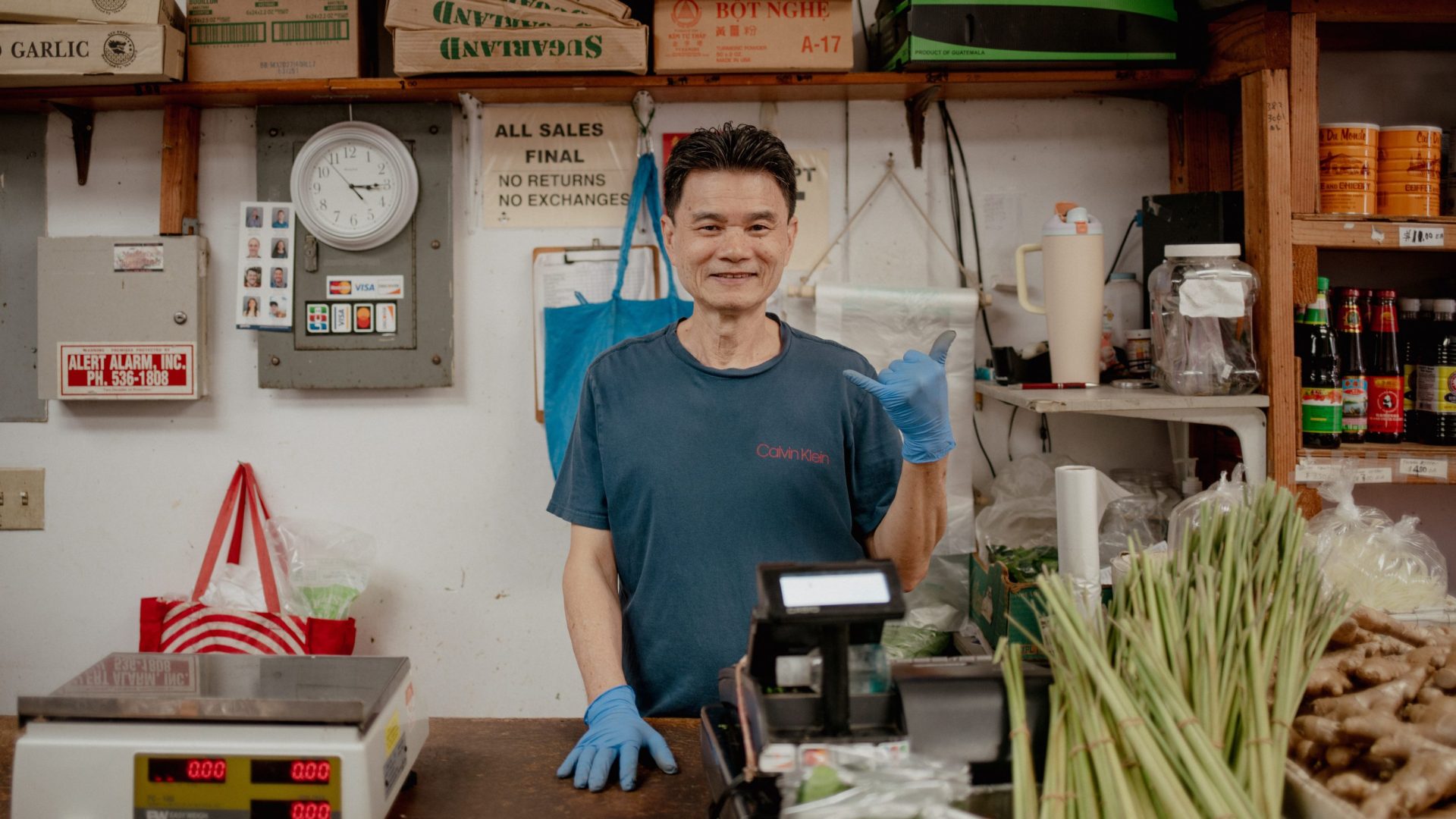 Man smiles from behind counter of store selling fresh market produce