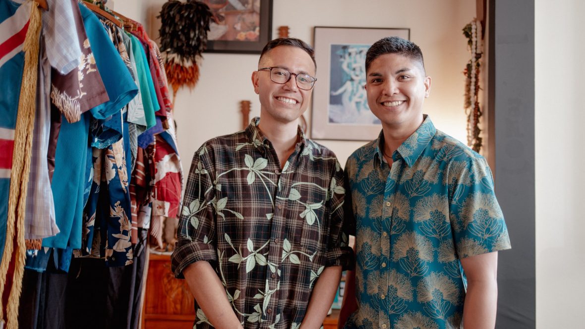 Two men wearing floral aloha shirts smile at camera