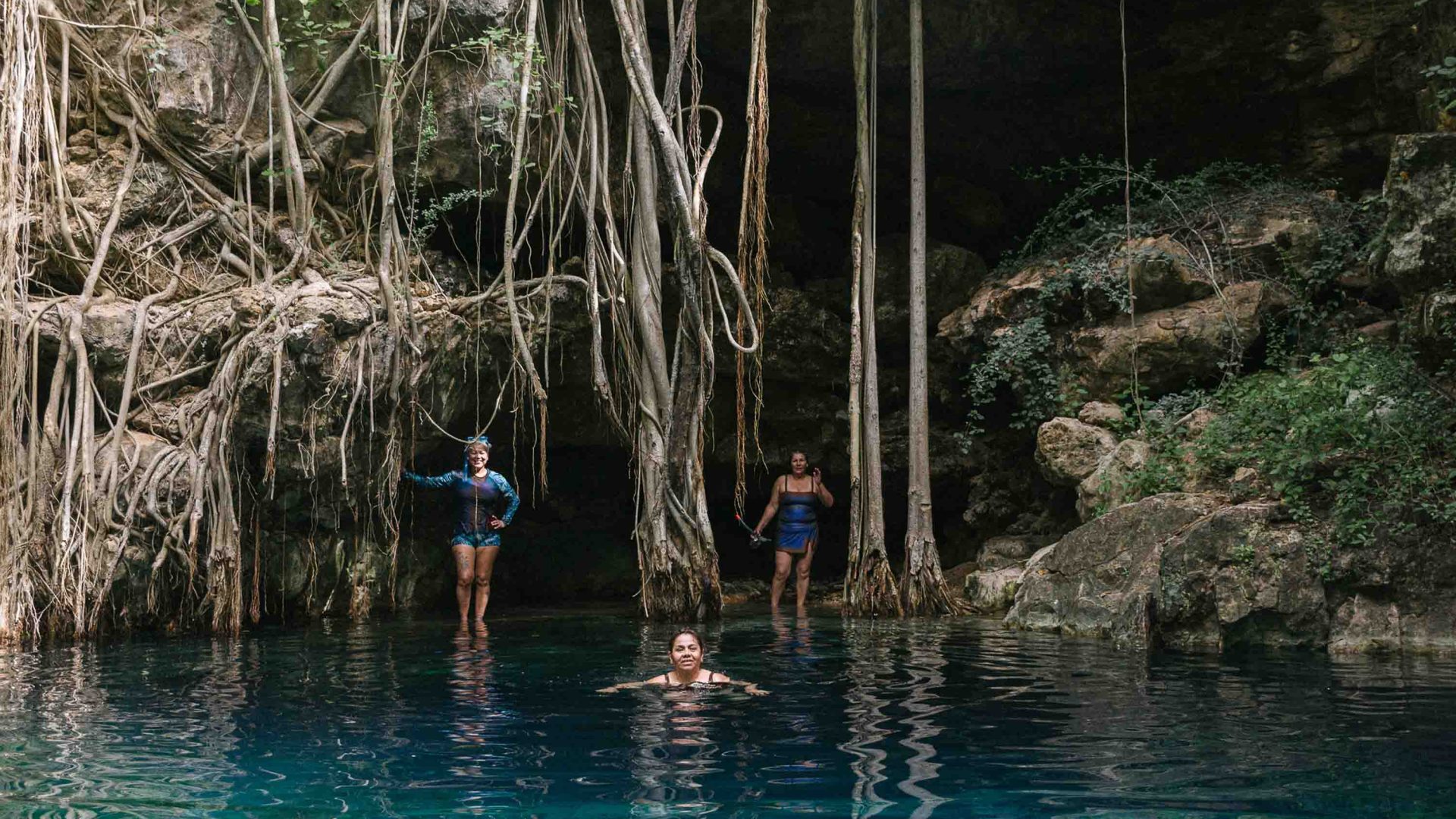 Three women swim in a wave with blue water.