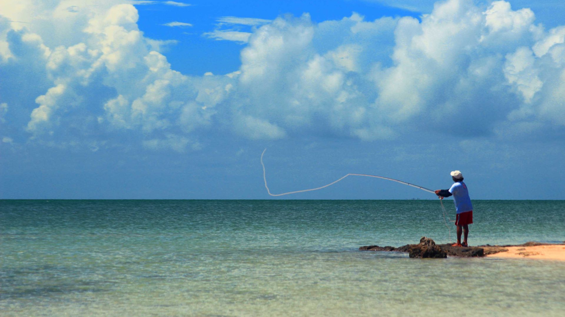 A man stands on a rock by the sea to fish.