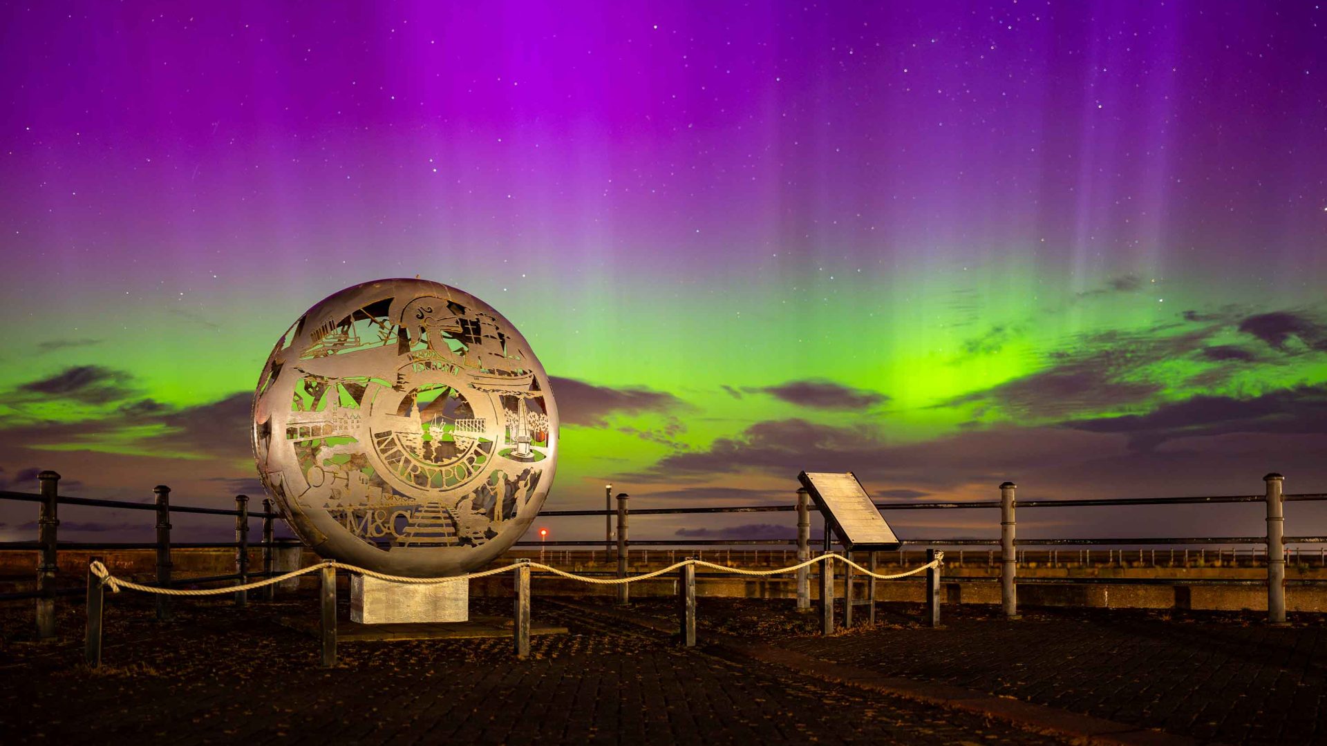 A purple and green sky behind a round, gold sculpture.