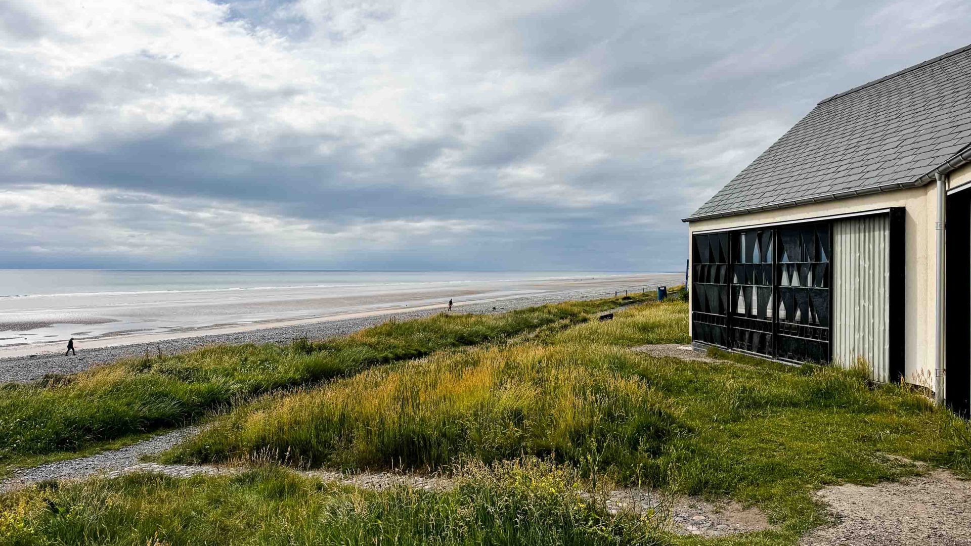 A building on the edge of a beach with just two people walking on it.
