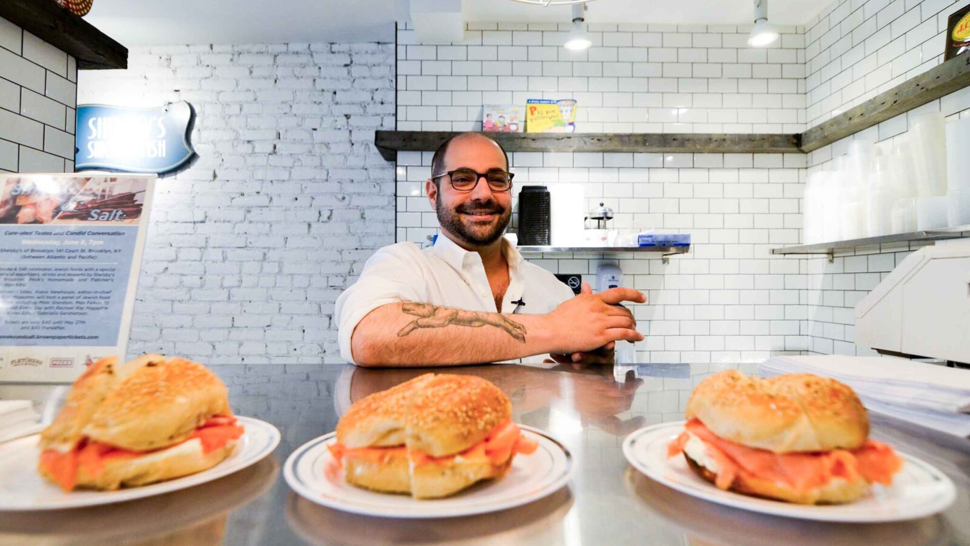 A man stands behind a counter top with salmon filled bagels on it.