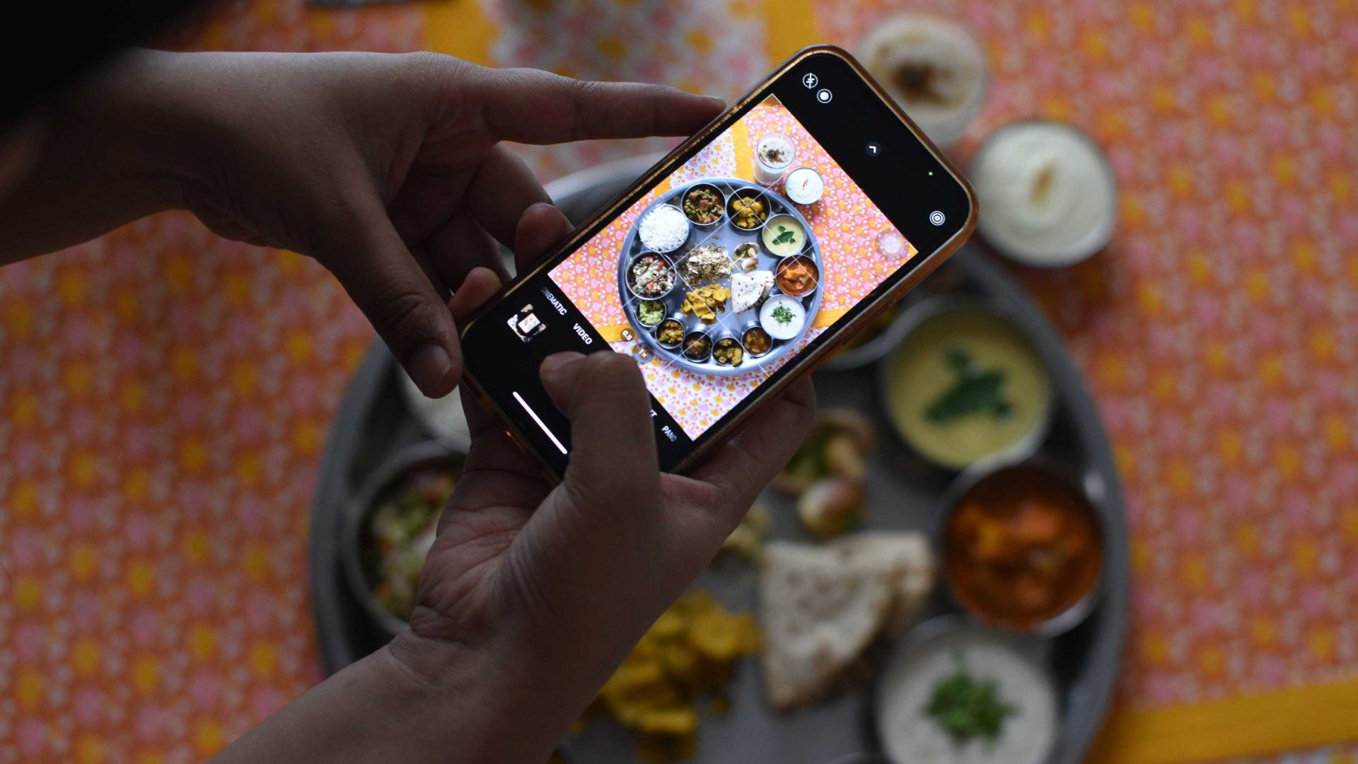 A phone held over a plate of Indian Thali.