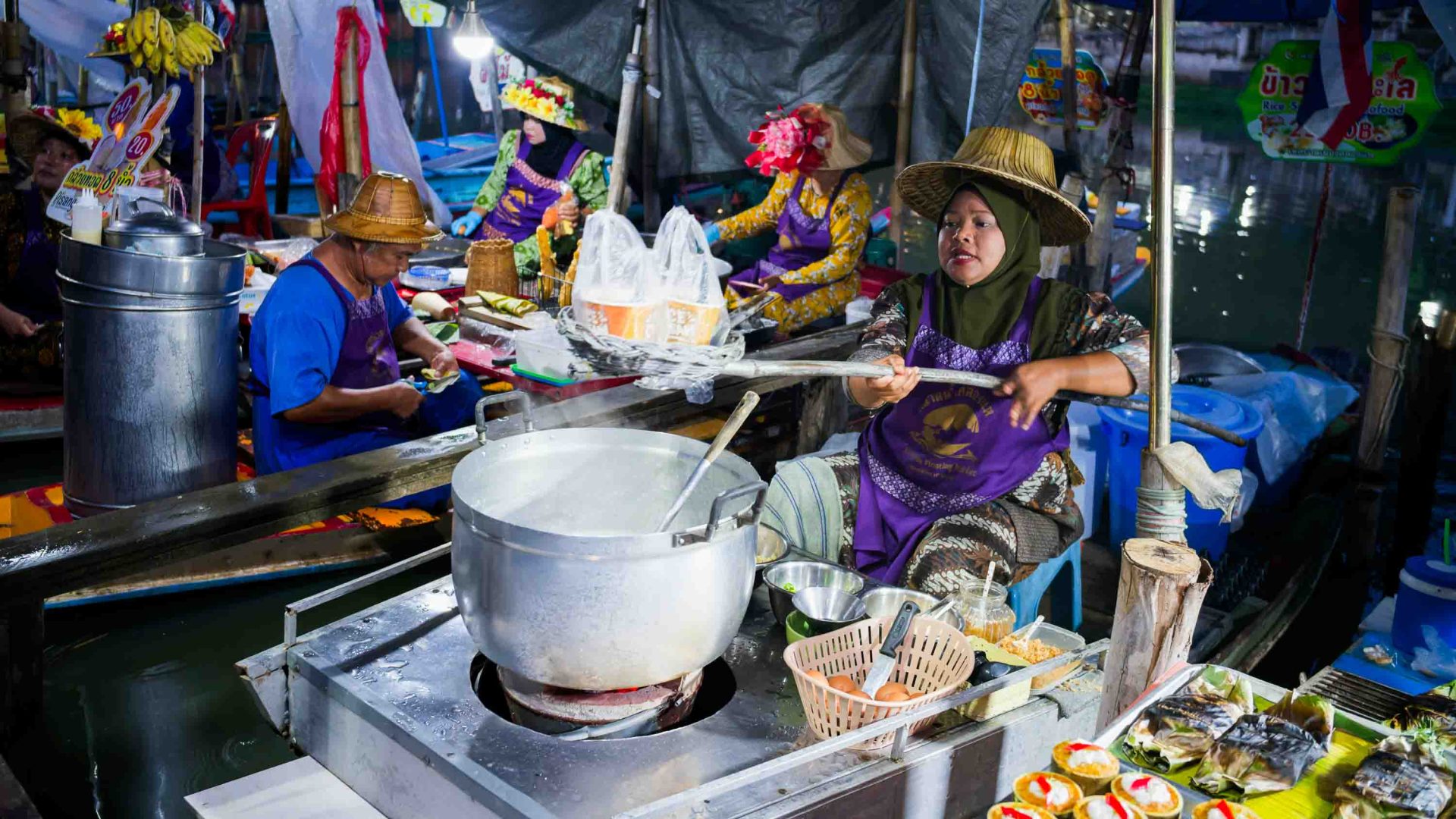 A woman in a hat makes food while seated at a big silver pot.