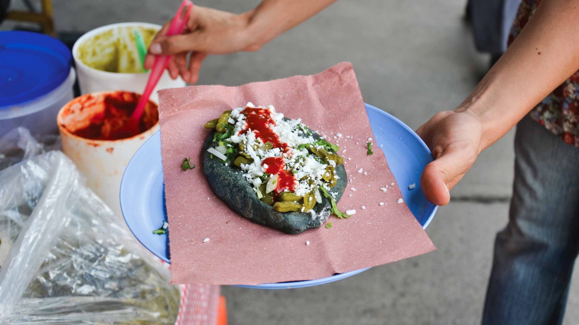 A hand scoops sauce onto a dish of food.