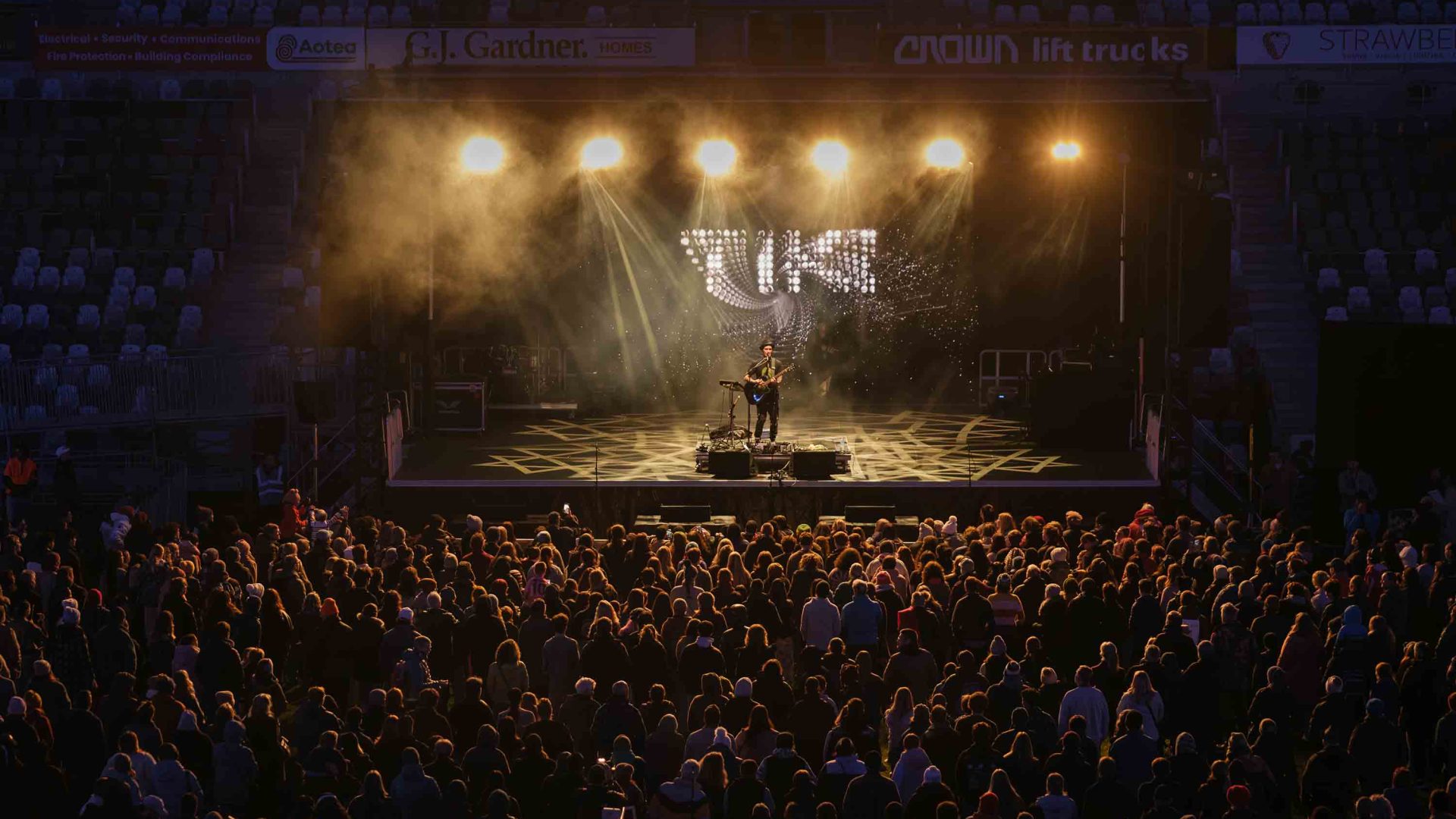 People watch a performer on an outdoor stage at night.