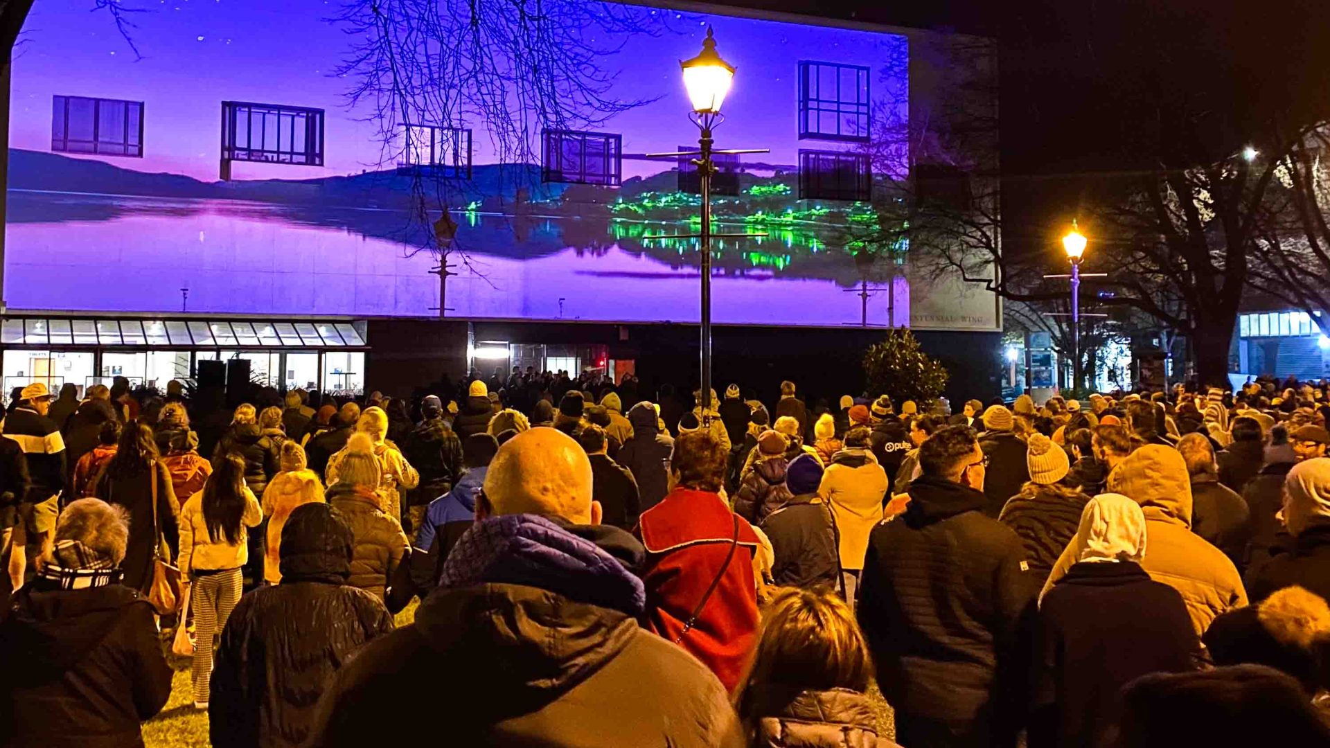 People watch a display on a screen outside.