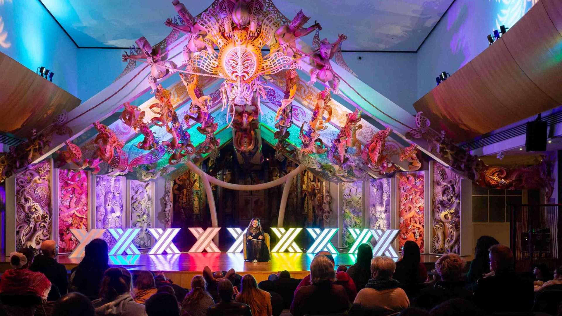 People watch a colourful performance on a stage.