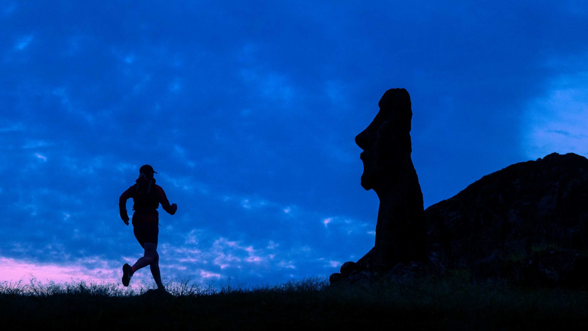The silhouette of a runner going past a stone statue.
