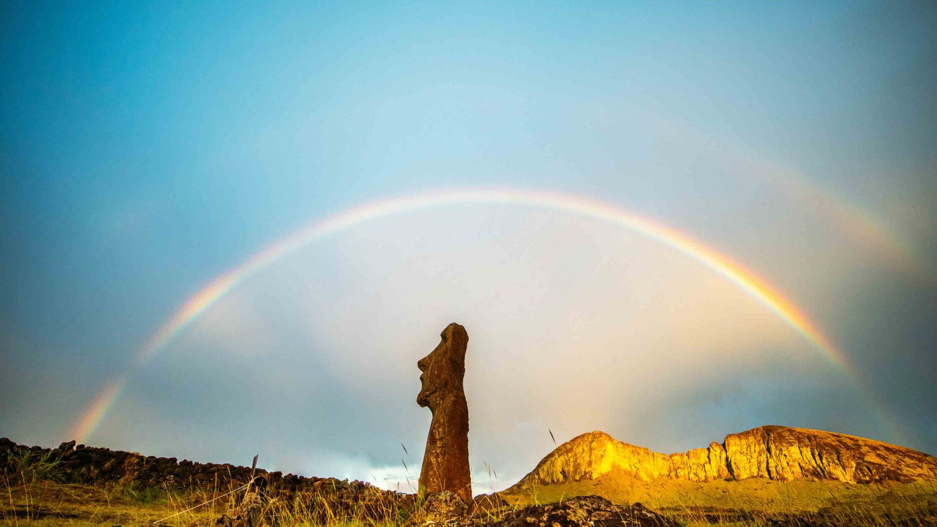 A double rainbow over a stone statue.