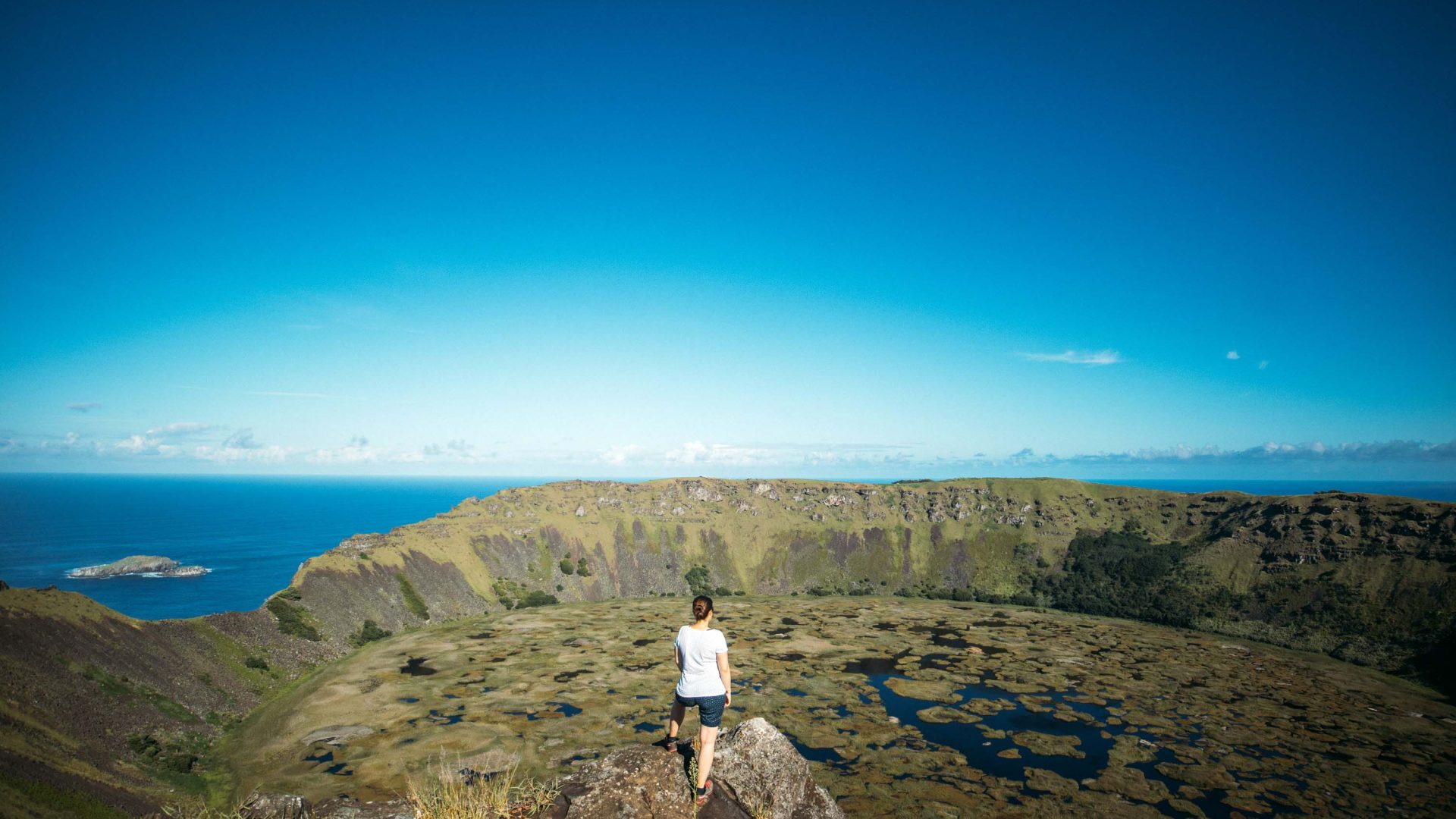 A woman stands on the rim of a volvanic crater looking out.