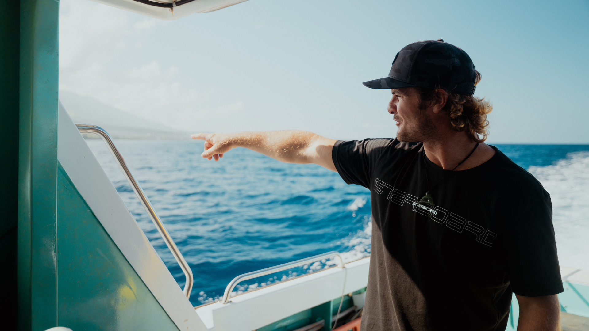 Man wearing black points to west Maui coastline.