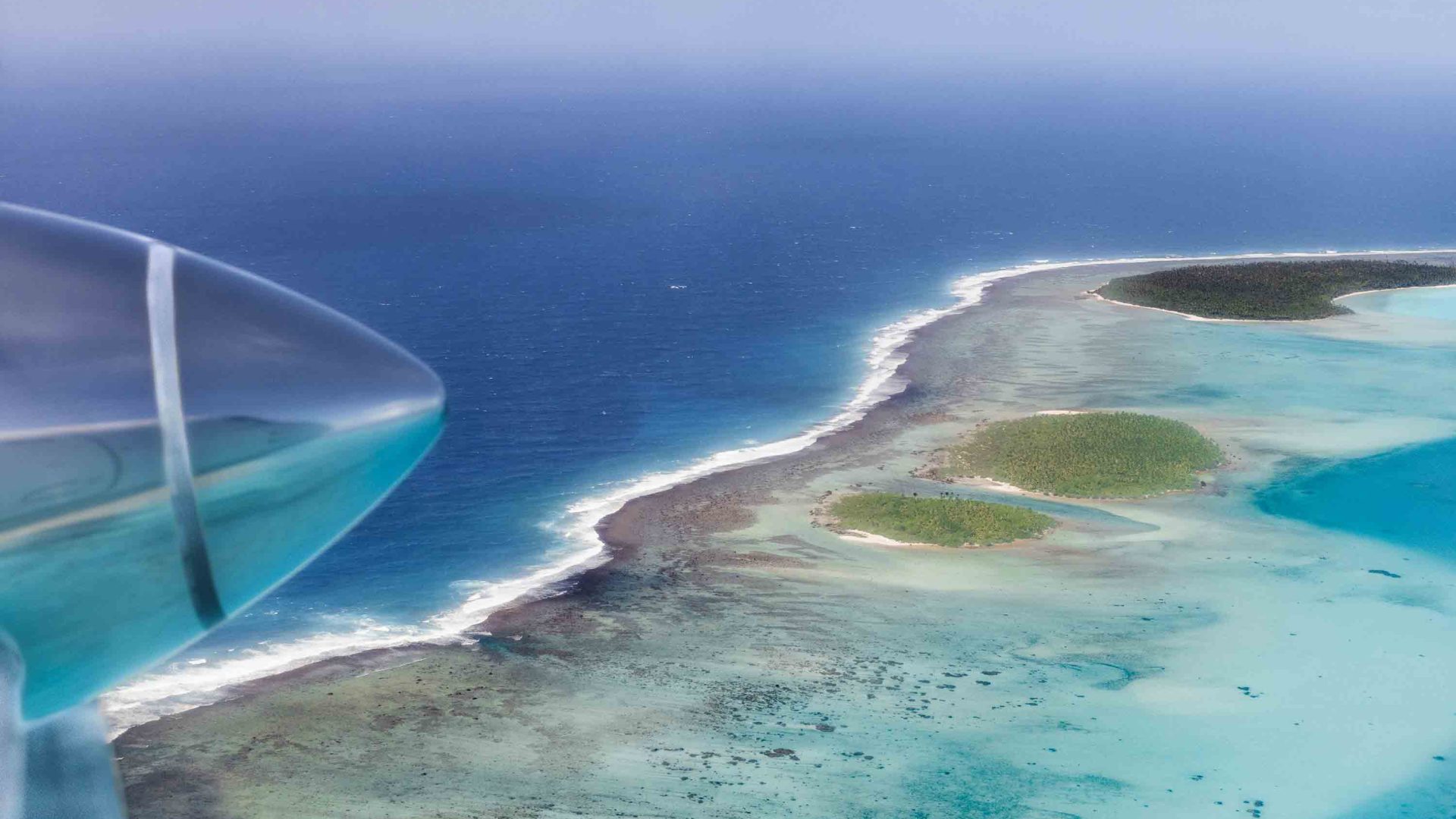 The jet of a plane is visible when looking down over island and sea.