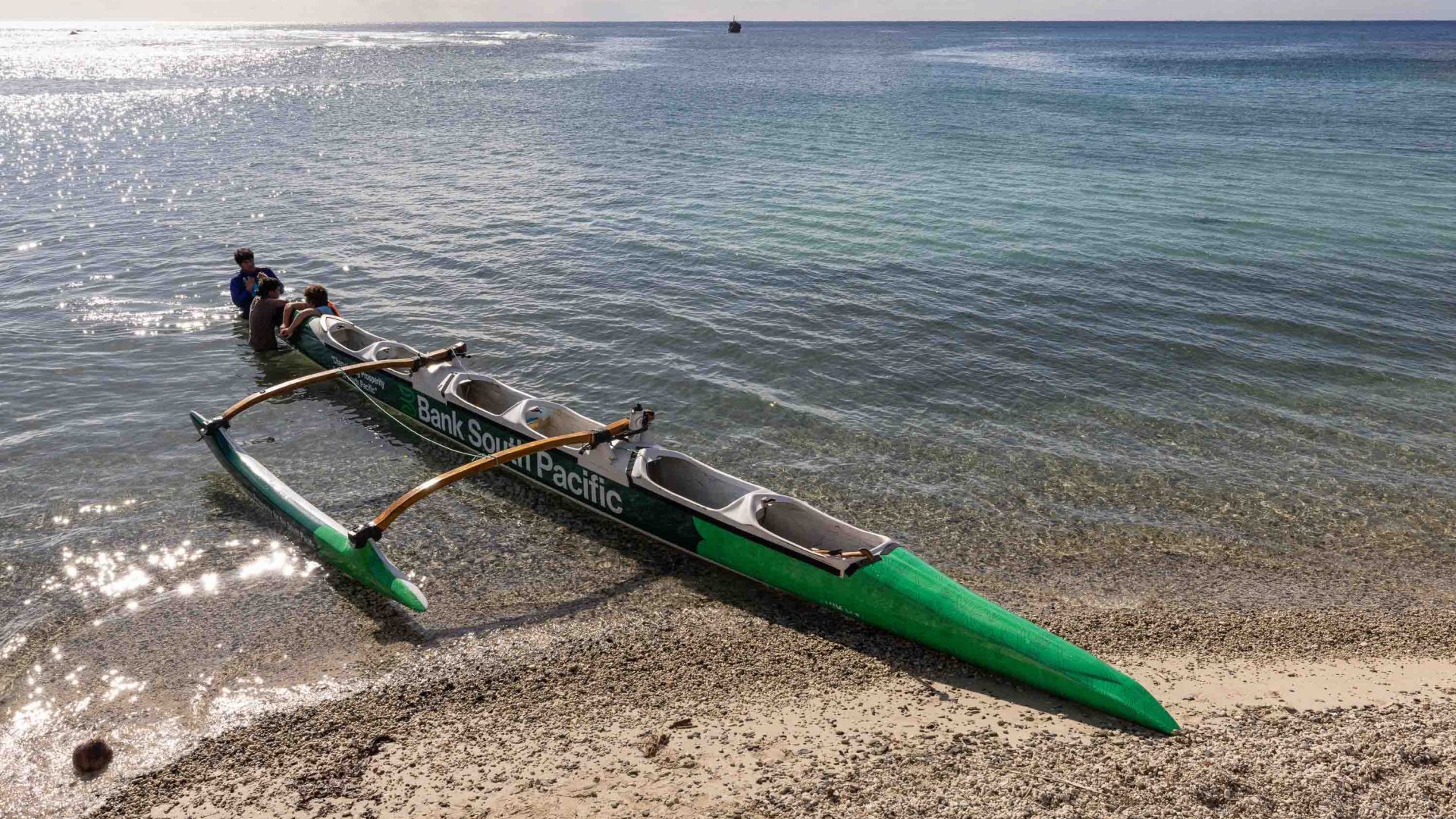 A green vaka canoe on the beach.