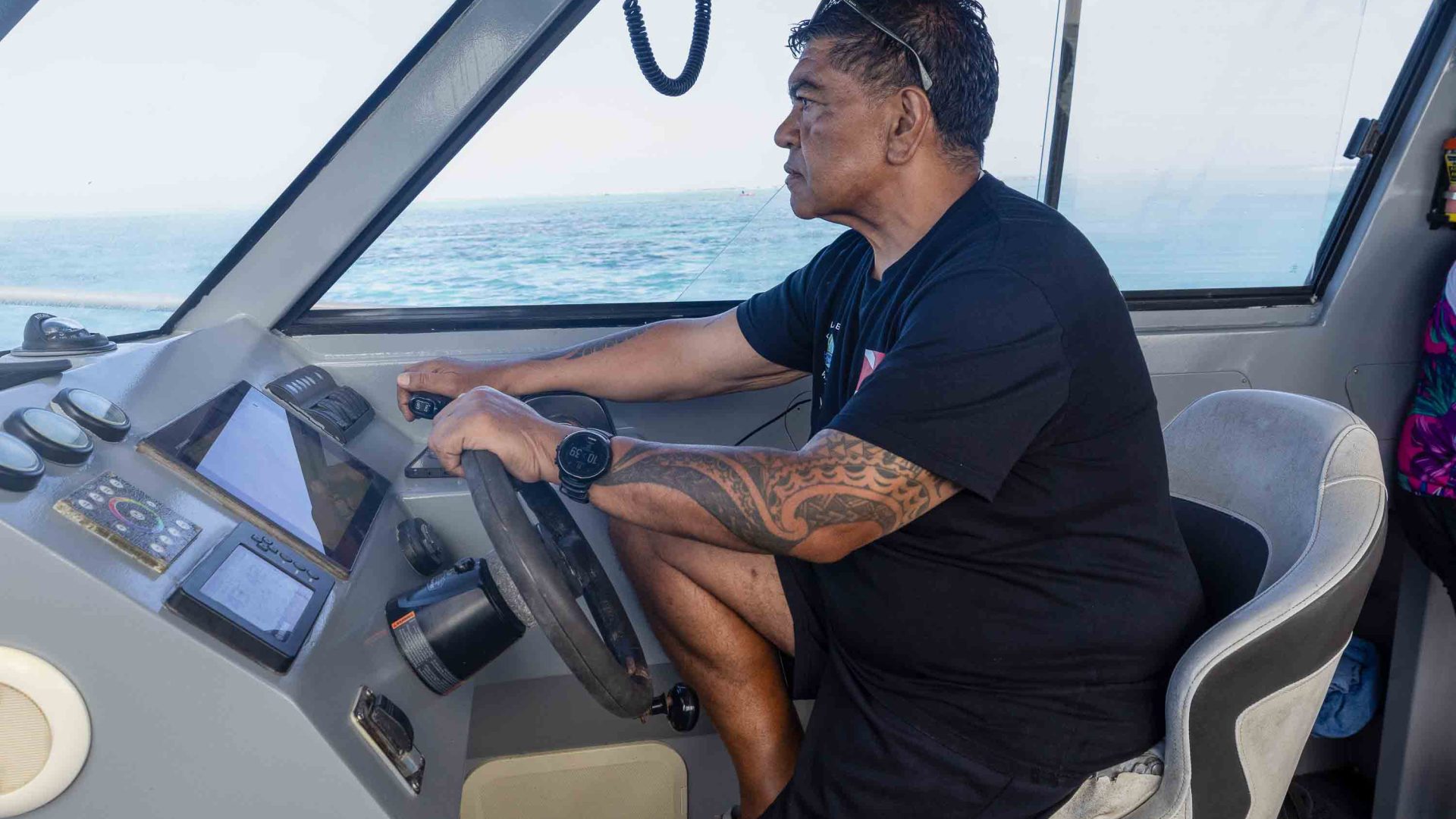 A man steers a boat. He looks straight ahead and is seen profile view.