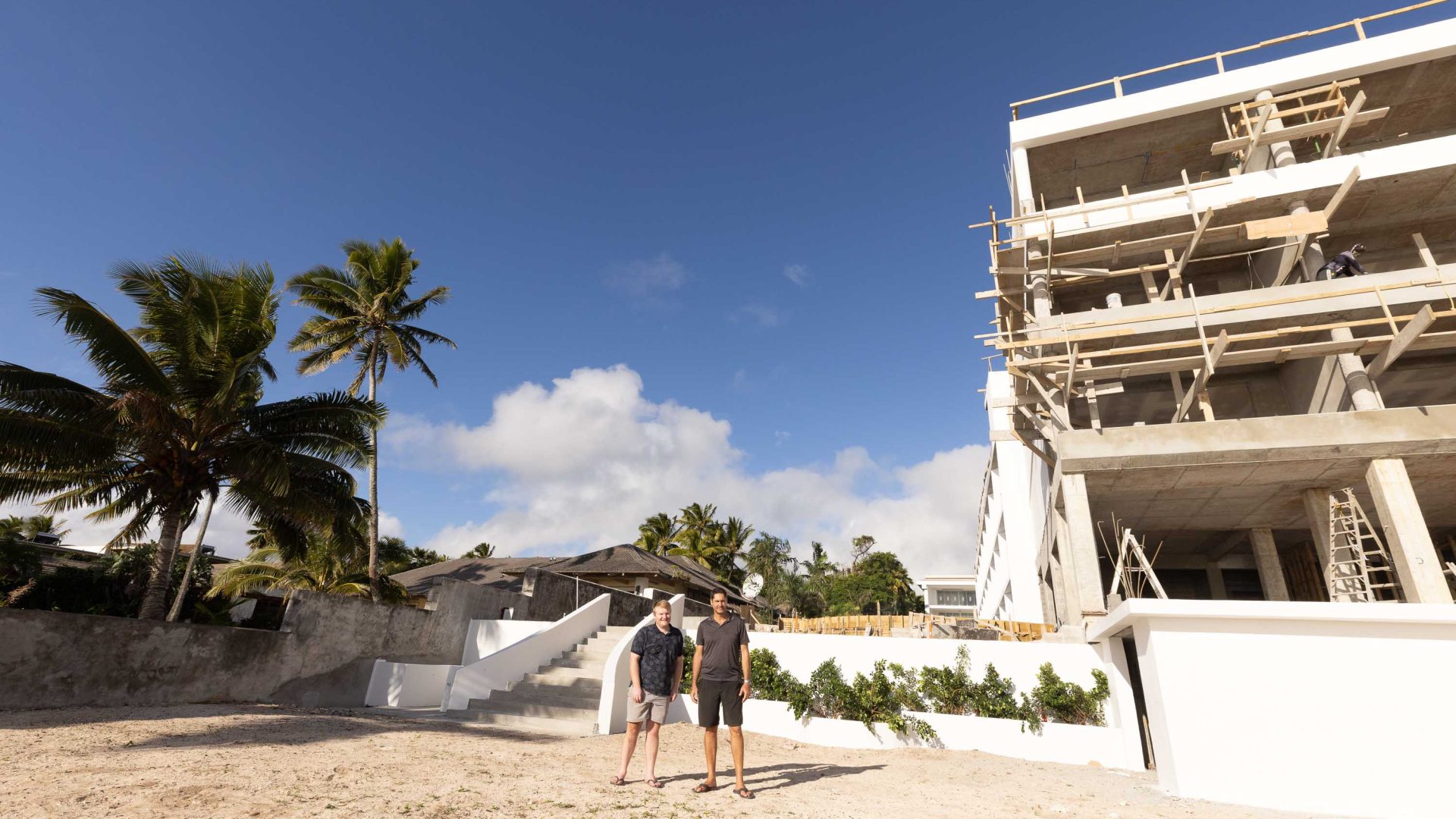 Two men stand at the building site of a hotel.
