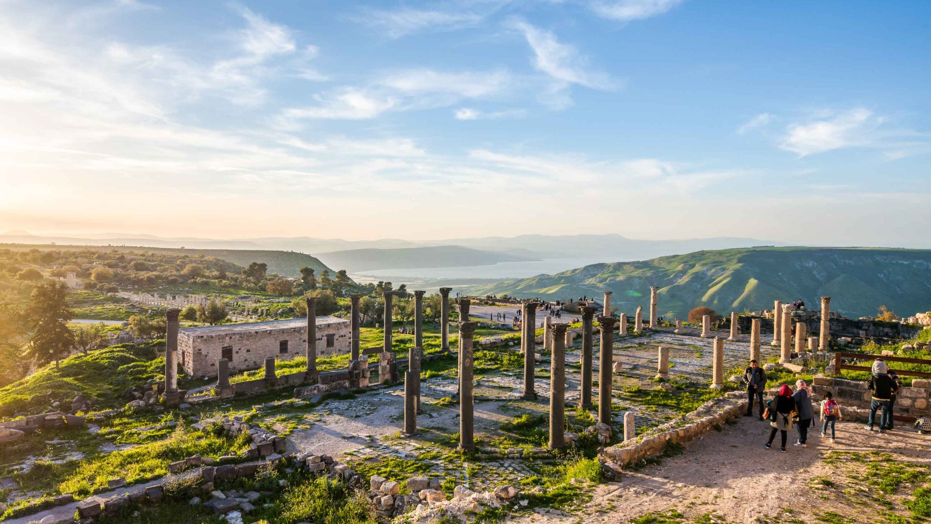 Ruins stand on a hill that drops down to the water.