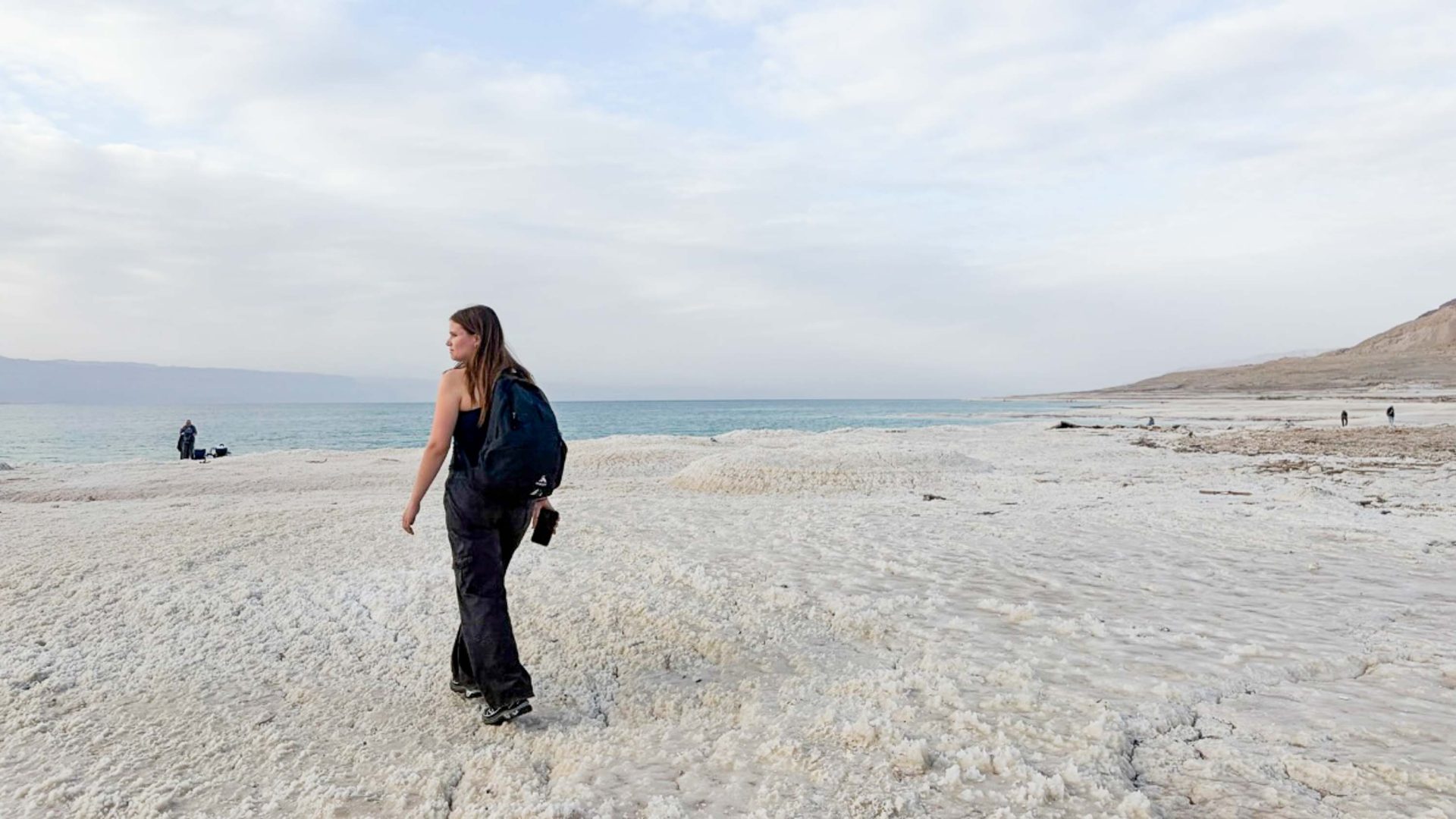 A woman walks across a white salty beach toward the water.