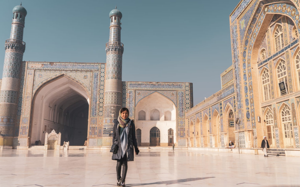 Woman wearing scarf stands beneath minarets.