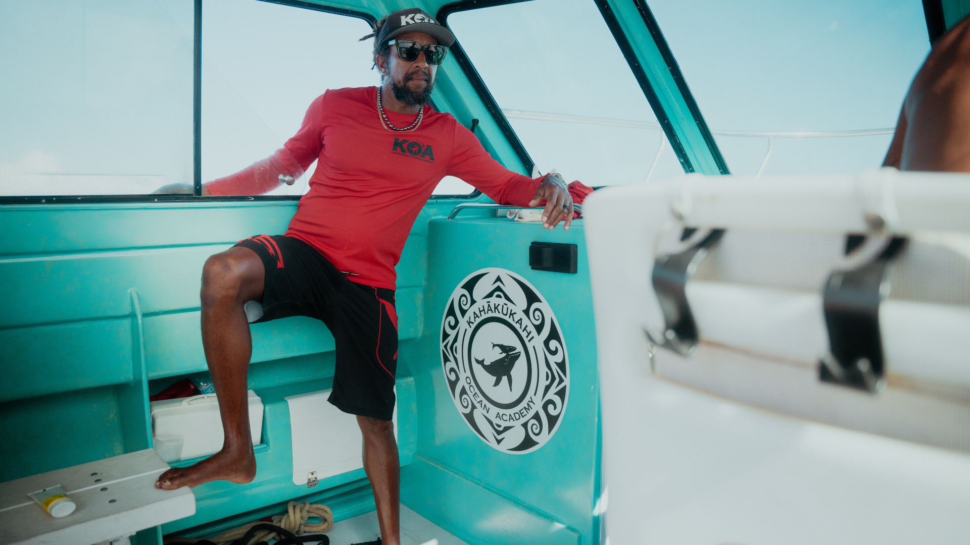 Man in red stands on light blue boat.