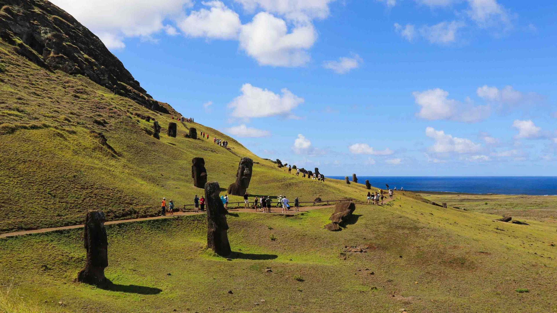 Tourists walk up a trail near stone statues.