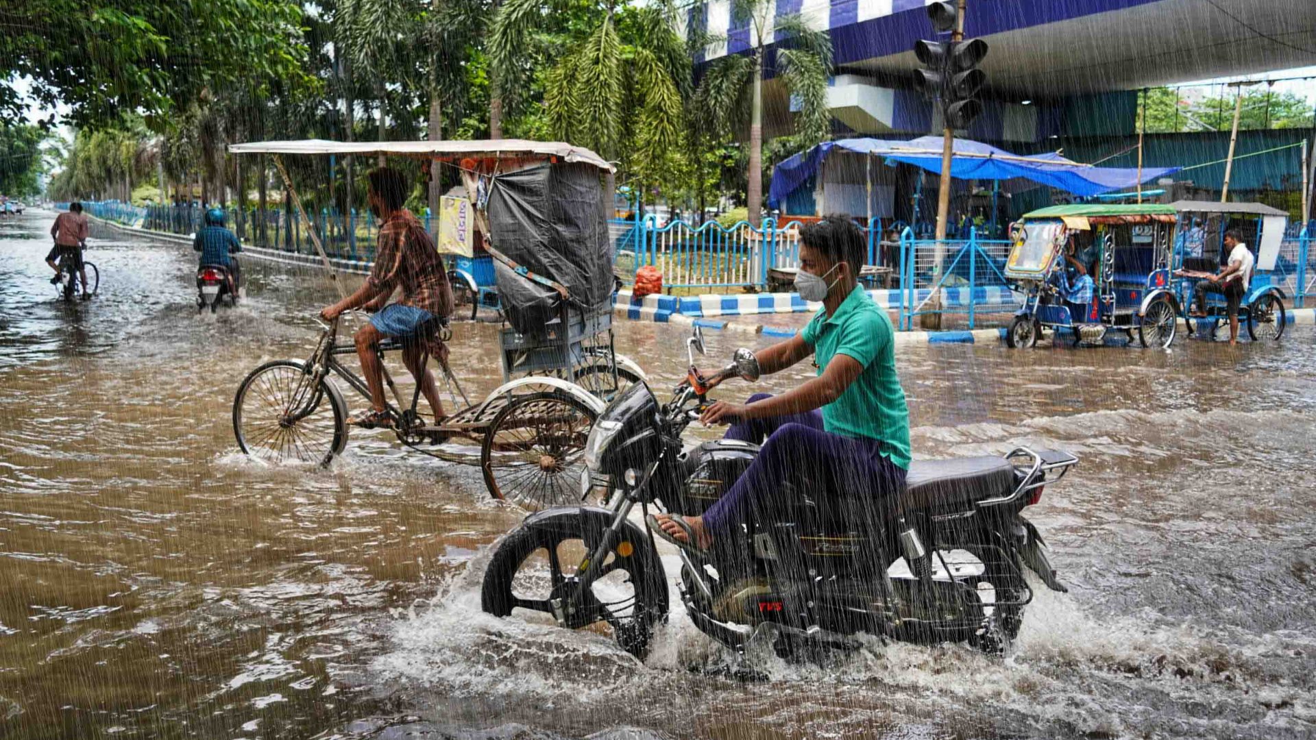 A motorcycle and a rickshaw try to navigate a flooded road.