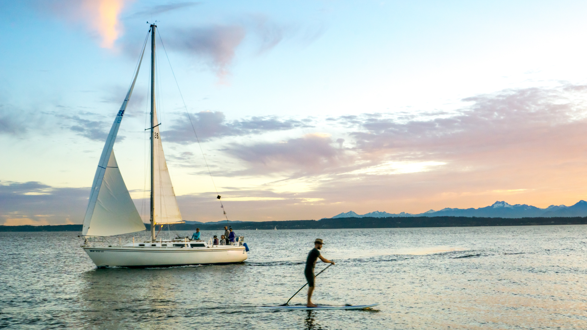 A sailboat and person on SUP against pink and blue sky