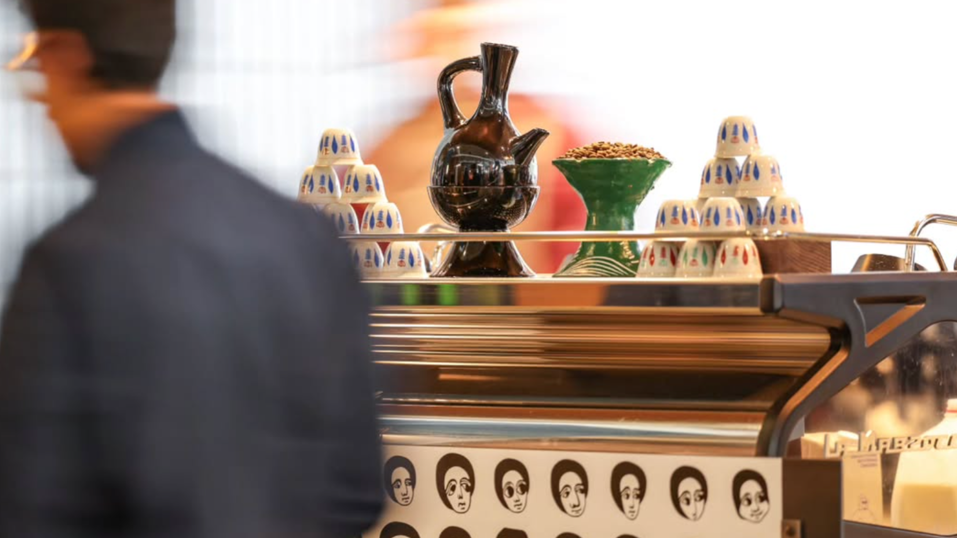 Man walks past coffee machine topped with traditional Eritrean coffee pot
