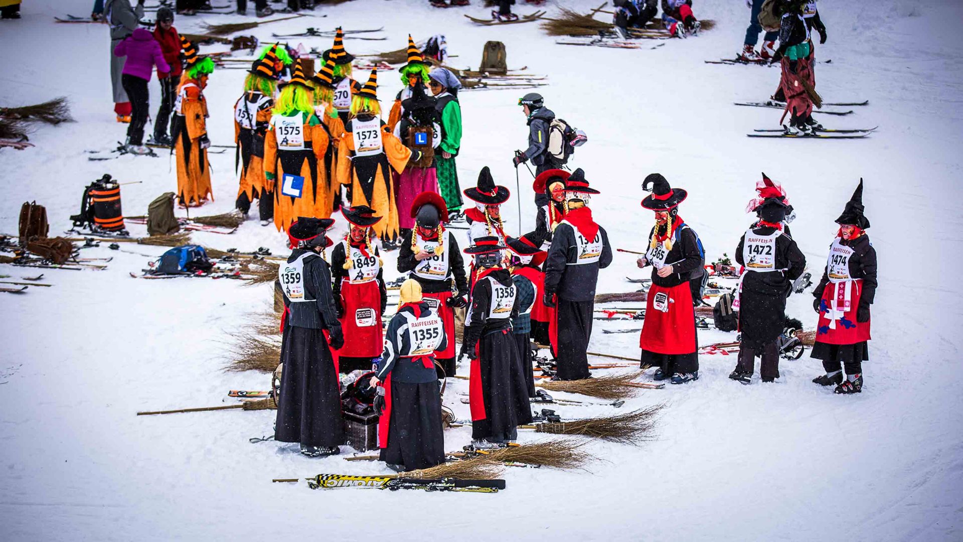 A group of people dressed as witches congregate on the snow.