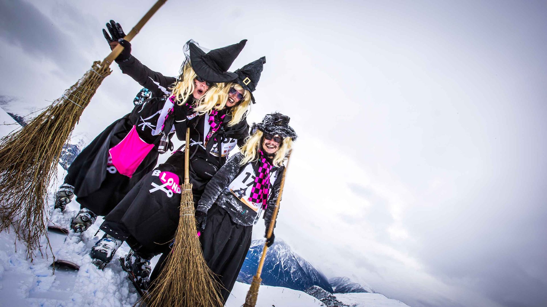 A group of people dressed as witches smile for a group photo with their witches broomsticks.