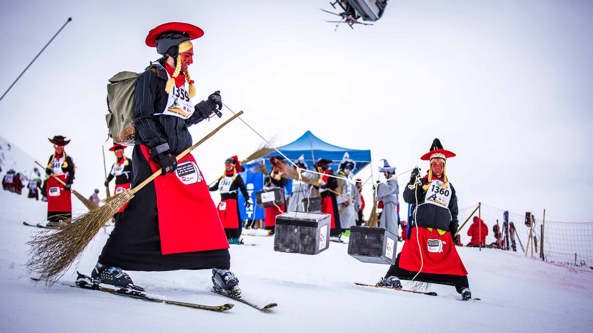 A couple of people dressed as switches take off down a snowy slope while other similarly dressed people stand in the background.