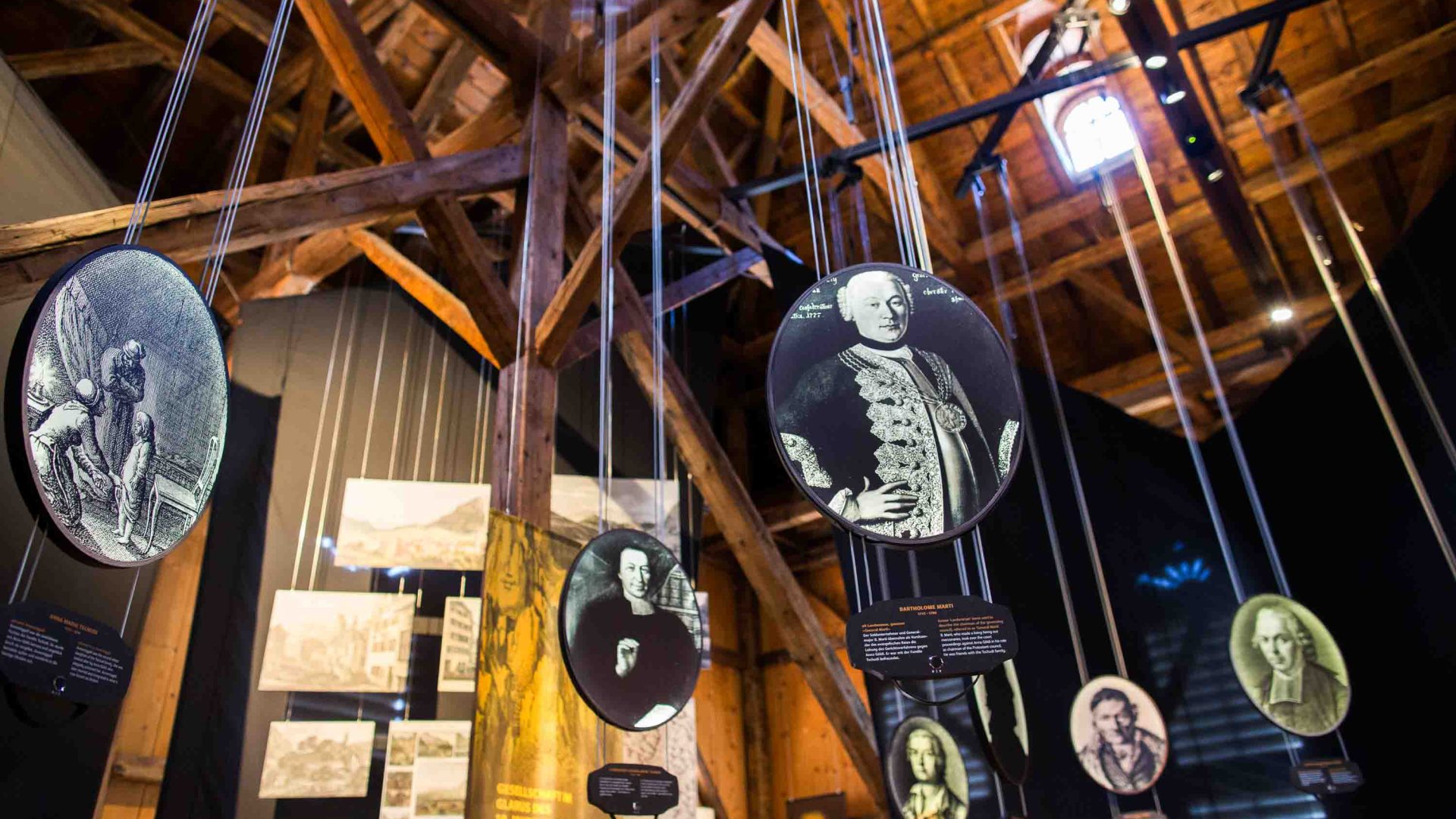 A museum display of suspended circular black and white portraits, hanging from wooden beams.