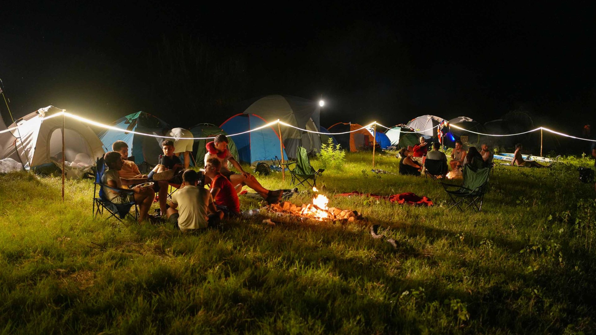At night campers sit by fires and tents are illuminated by small lights.