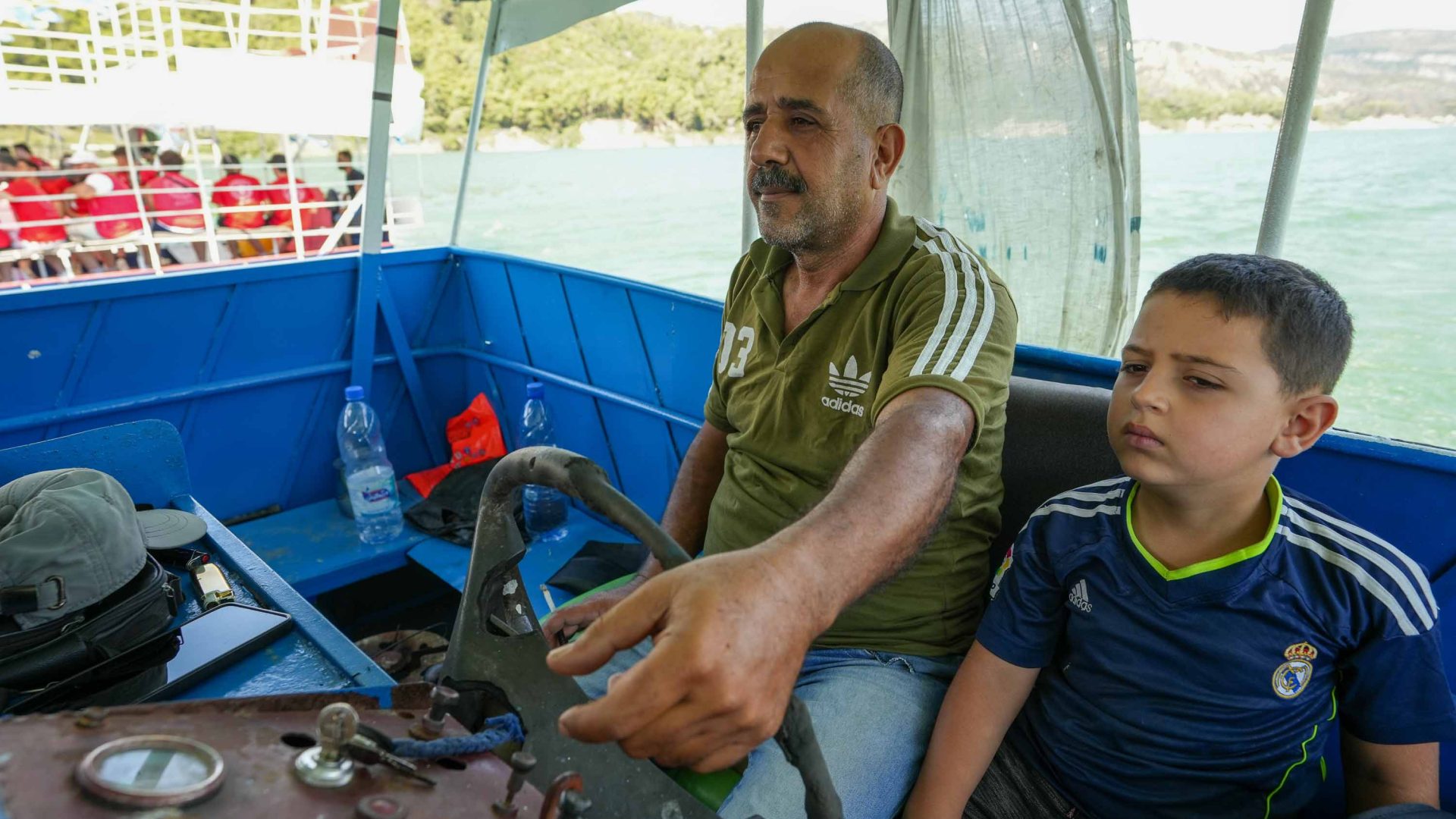 A man drives a boat while a young boy sits beside him.