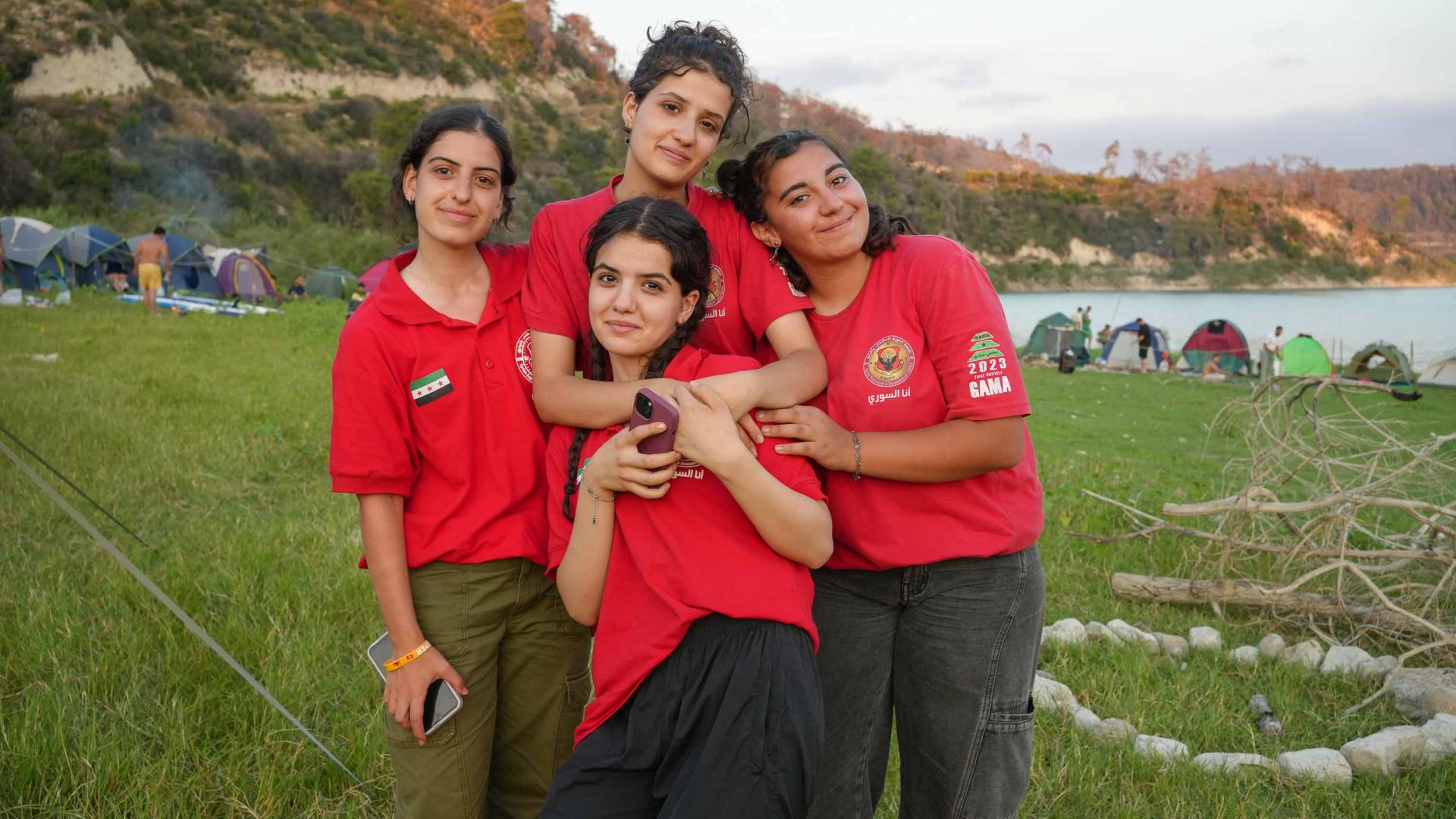 Four girls smile for a group photo at a campsite.