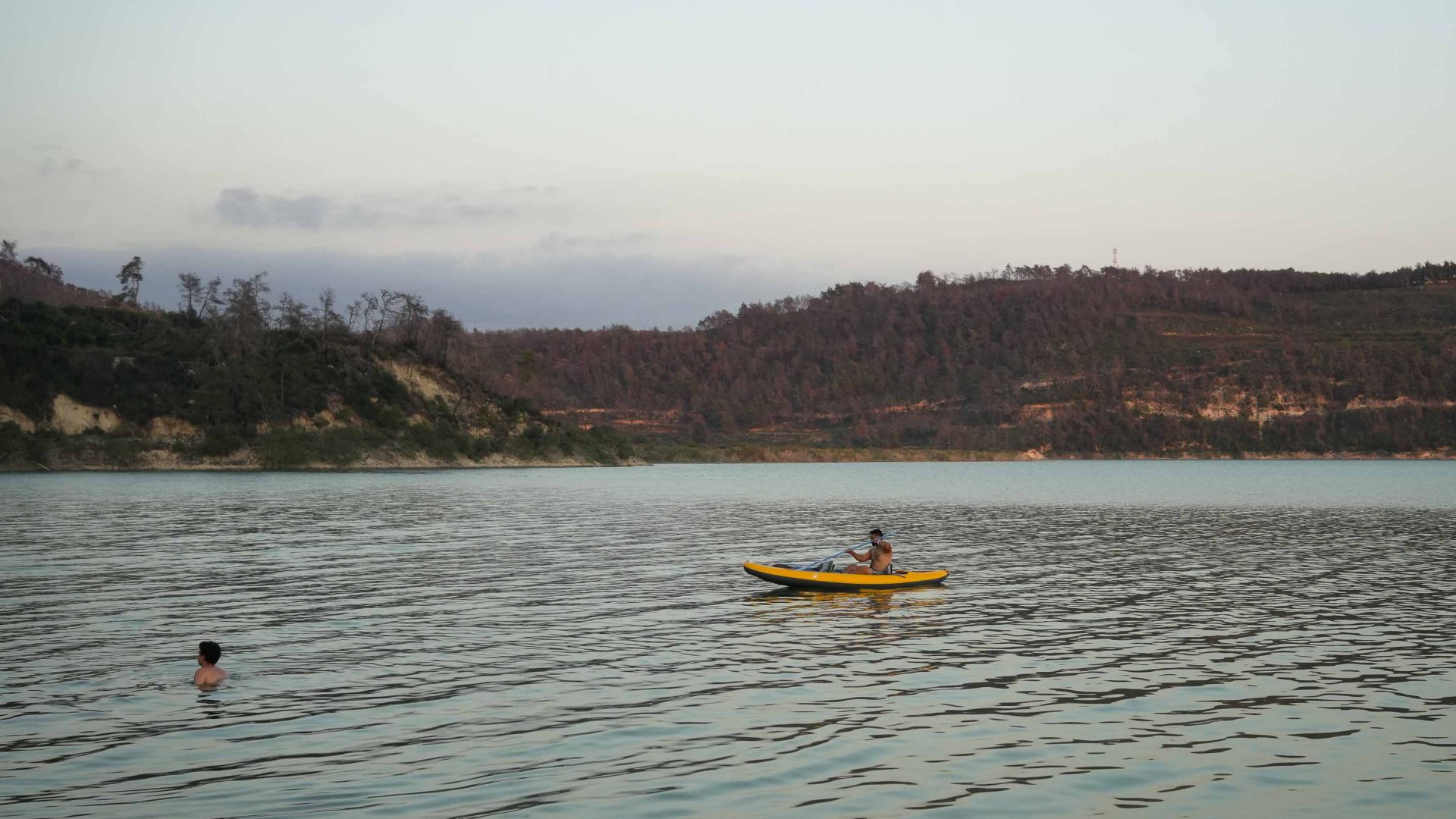 A camper kayaks while another swims in the lake.