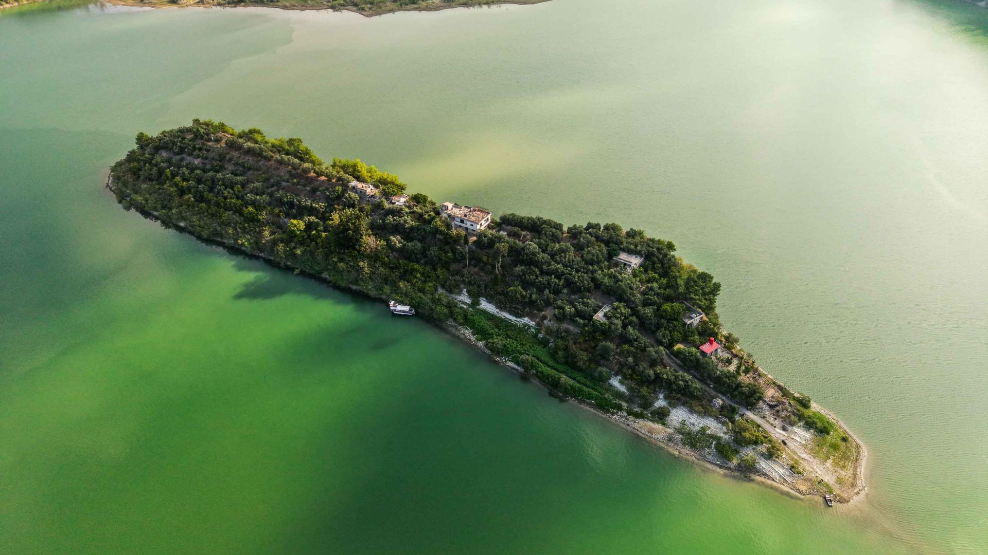 A drone photo of a small long island in a lake, covered by trees.