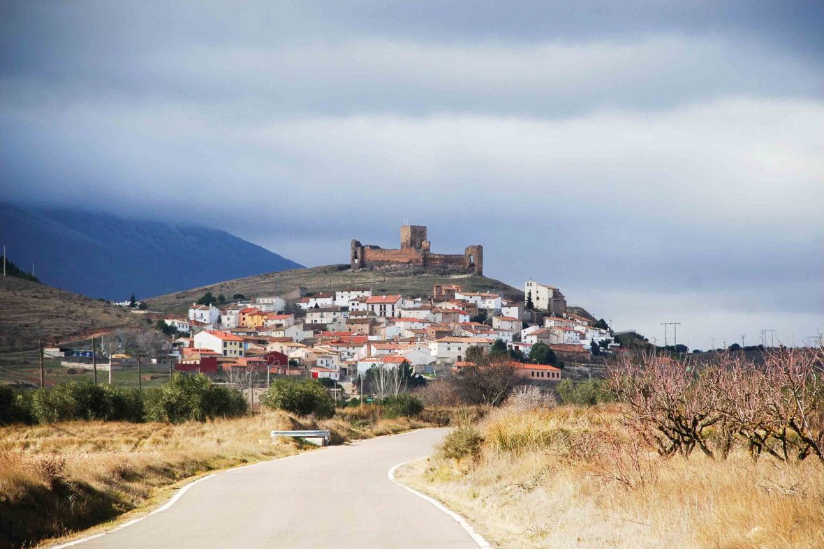 A road leads up to a town with a castle perched on the hill above it.
