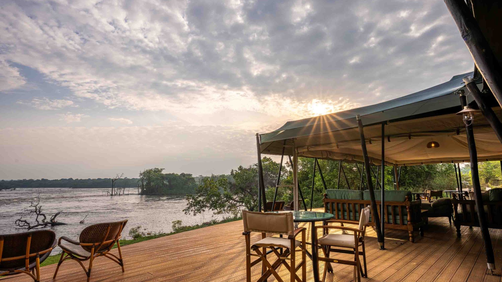 A tent above a deck with seats overlooks a river.