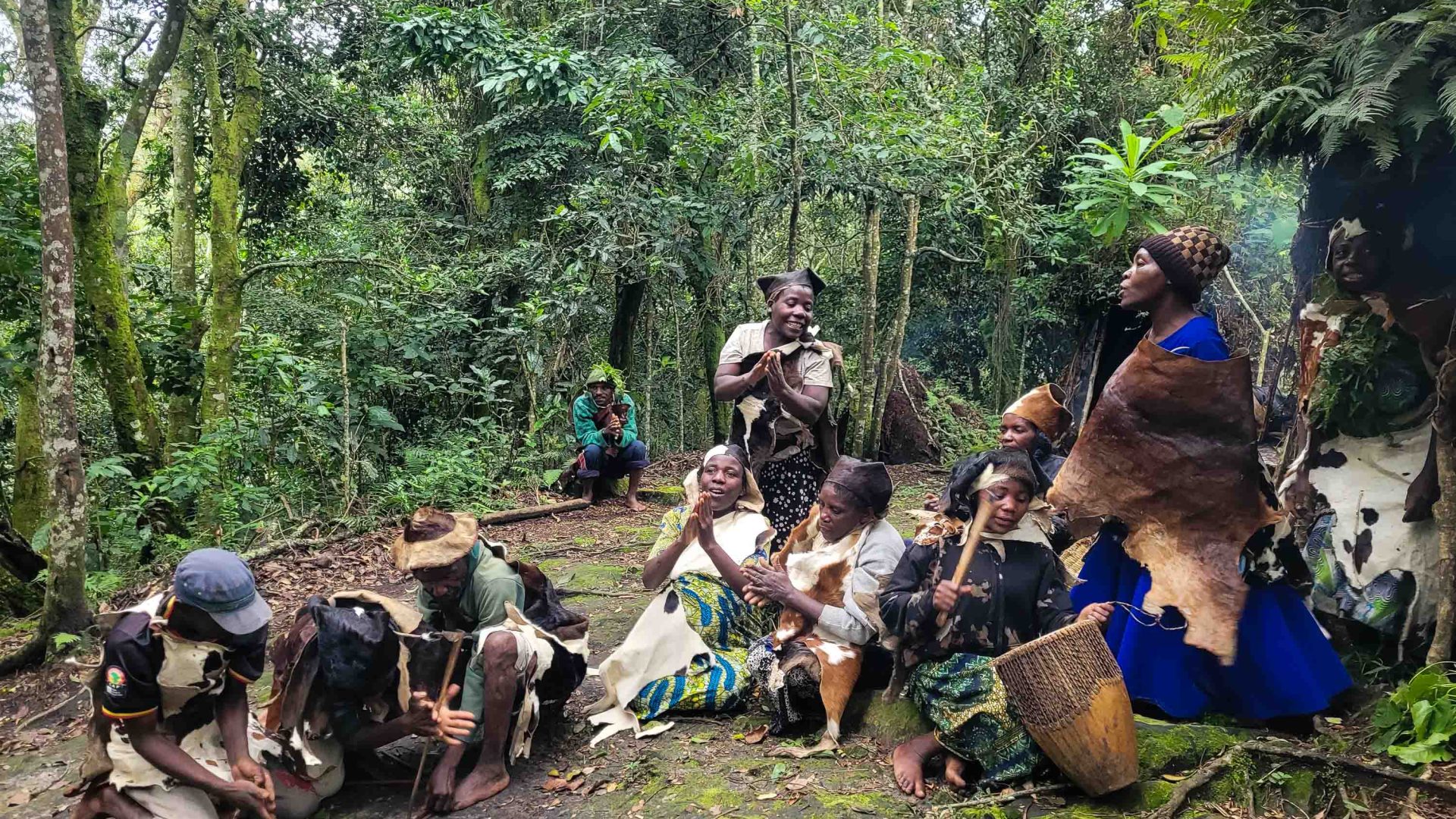 A group of women sit on the ground in a forest setting.